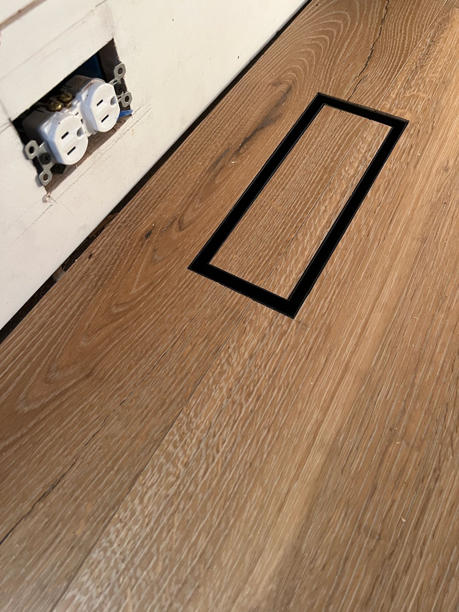 A wooden floor with a hole in it and two electrical outlets.