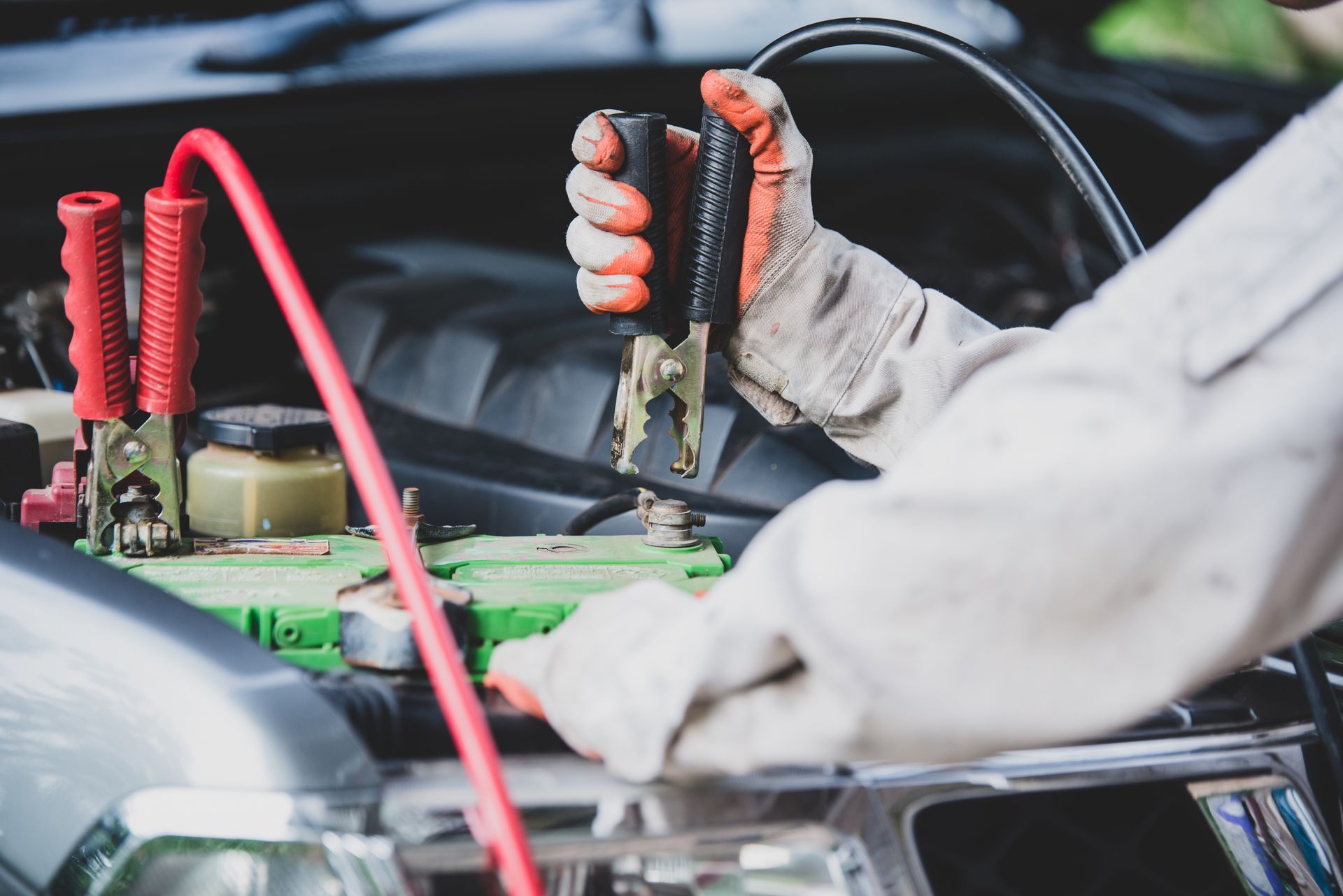 Person using jumper cables to jump-start a car battery under the hood.