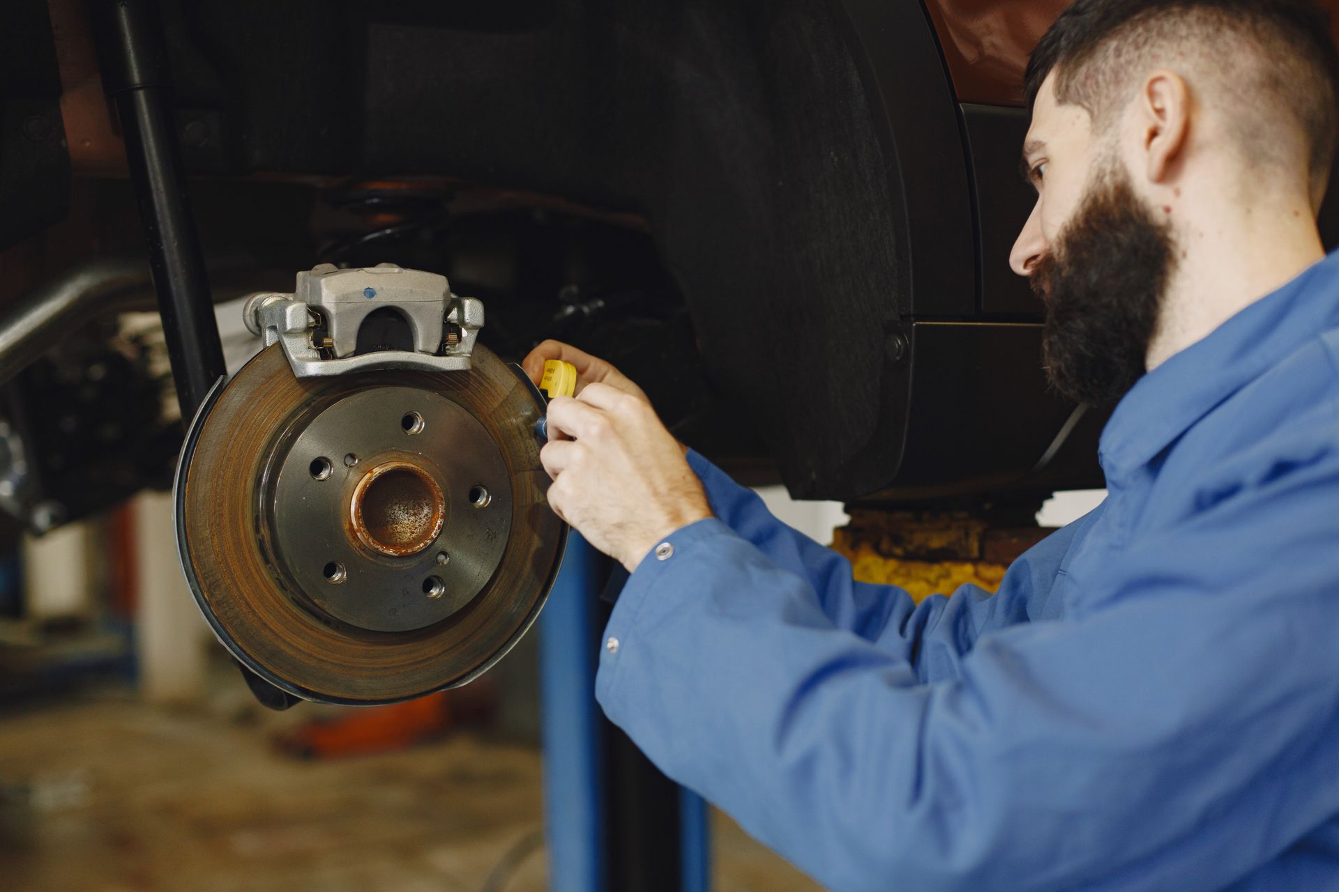 Mechanic in blue overalls working on a car's brake rotor in a garage.