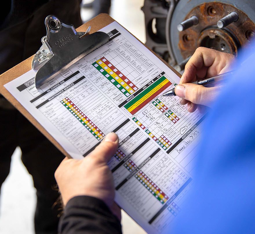 Mechanic inspecting a car, filling out an inspection checklist on a clipboard.
