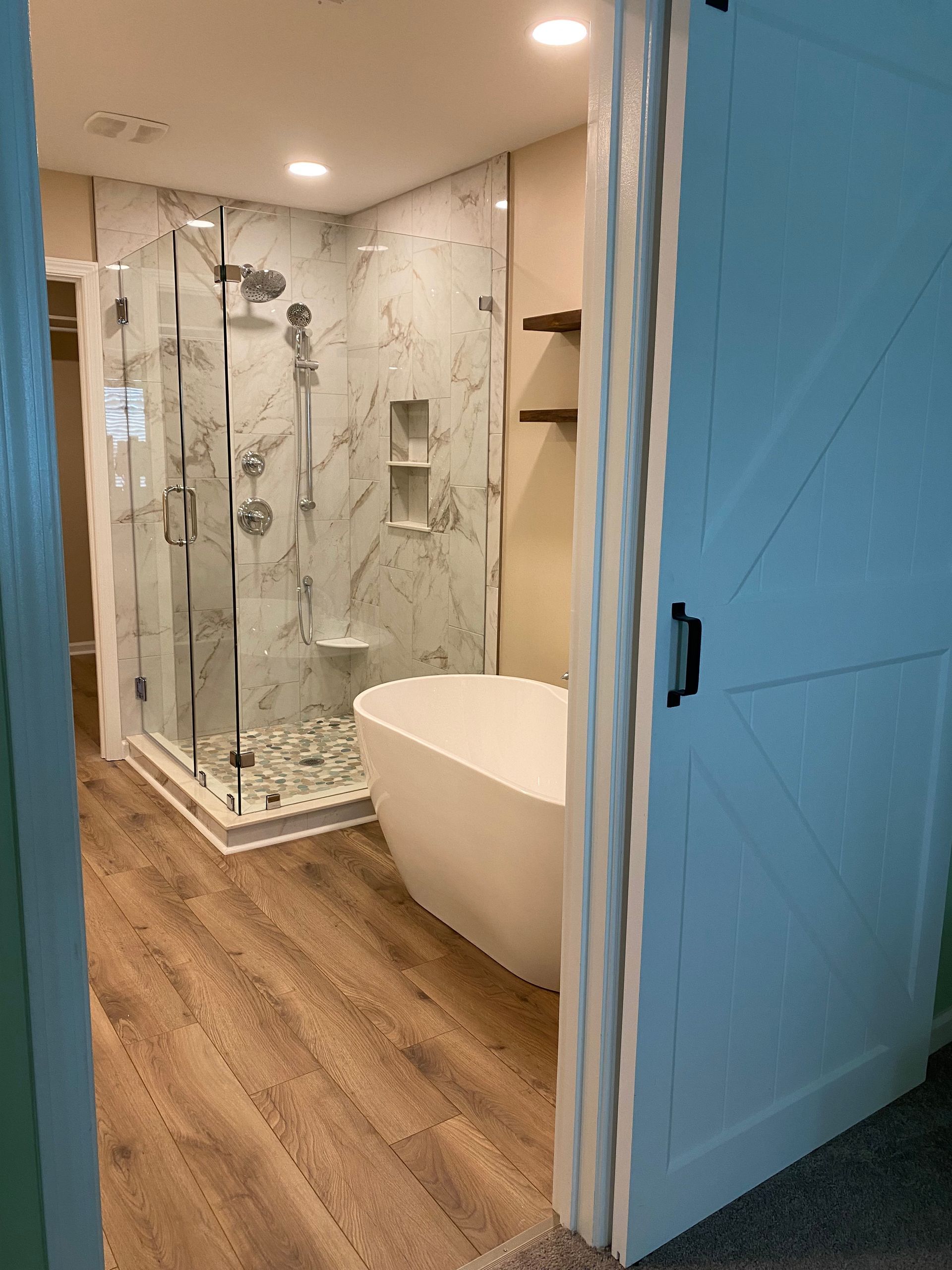 Barn-style sliding door leads to a bathroom with a walk-in tiled shower and freestanding tub.