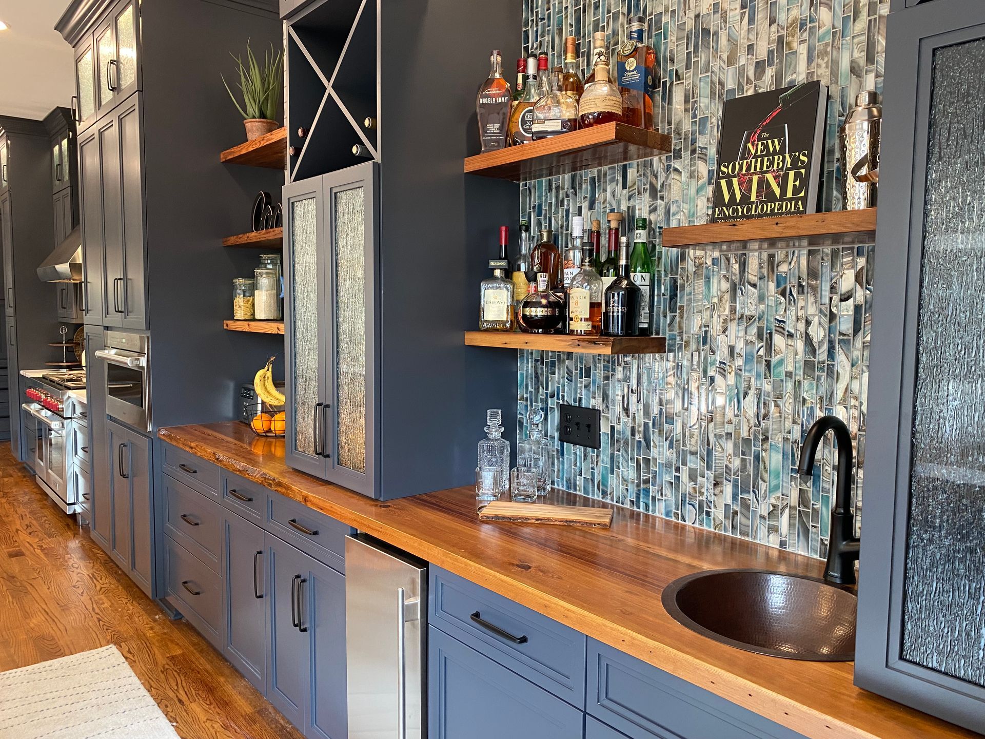 Wet bar with reclaimed wood countertop and floating shelves and mosaic blue, black, and white tile backsplash.