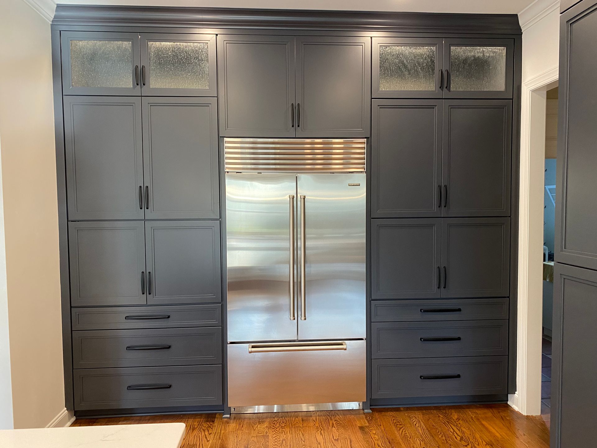 Built-in SubZero refrigerator surrounded by custom built dark blue pantry cabinets.