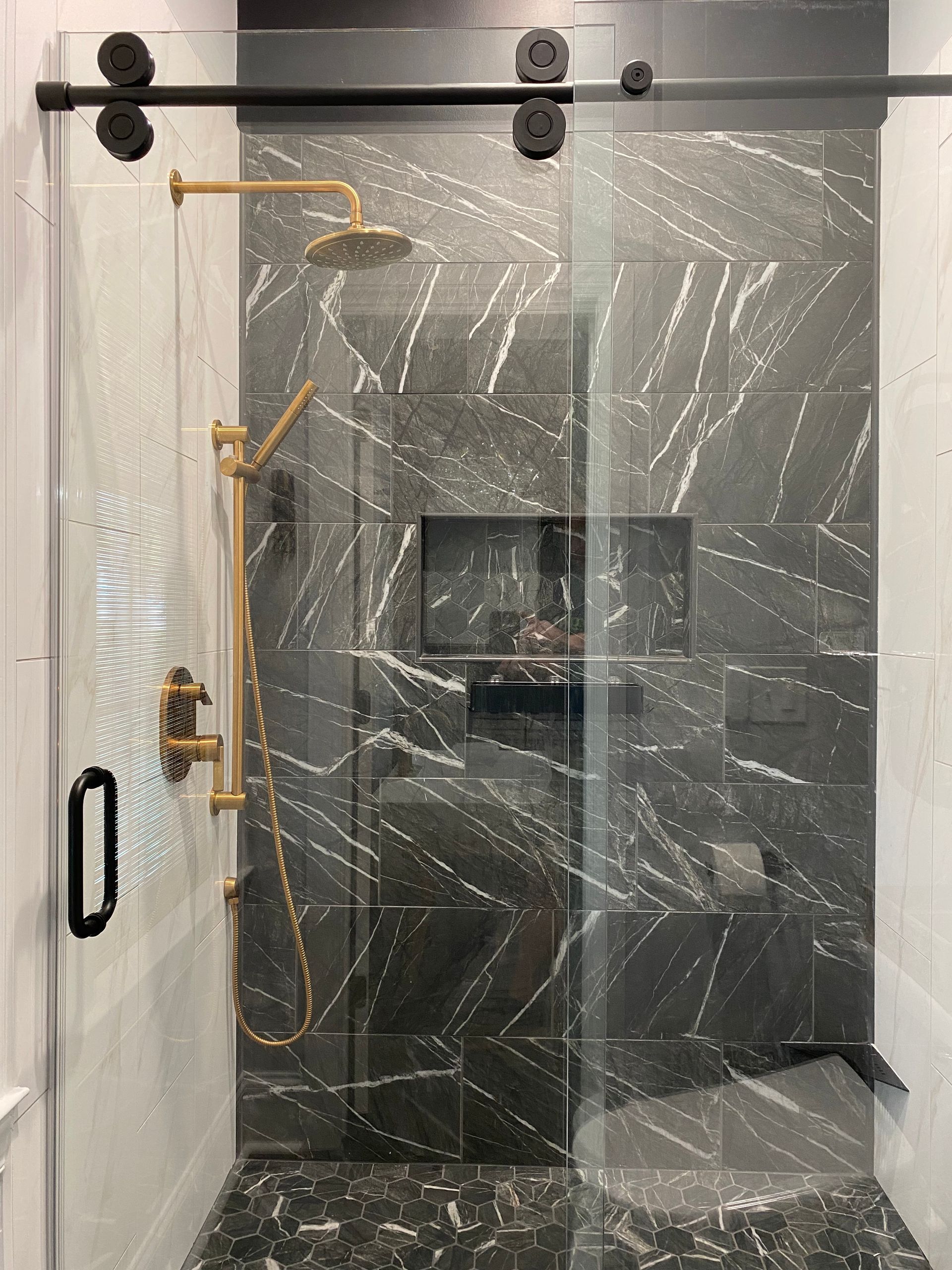 Black marbled tile shower with gold fixtures featuring a roller barn style shower door.
