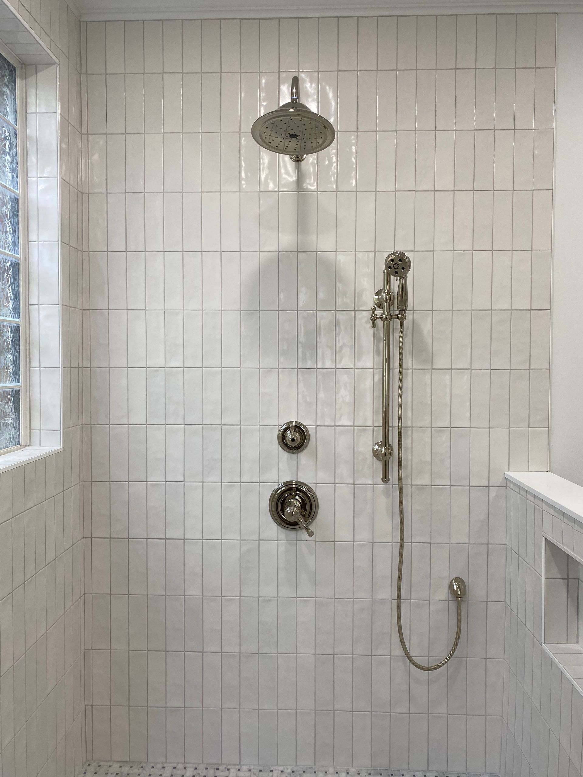 White vertical stacked tile shower with chrome handheld sprayer on slider. 