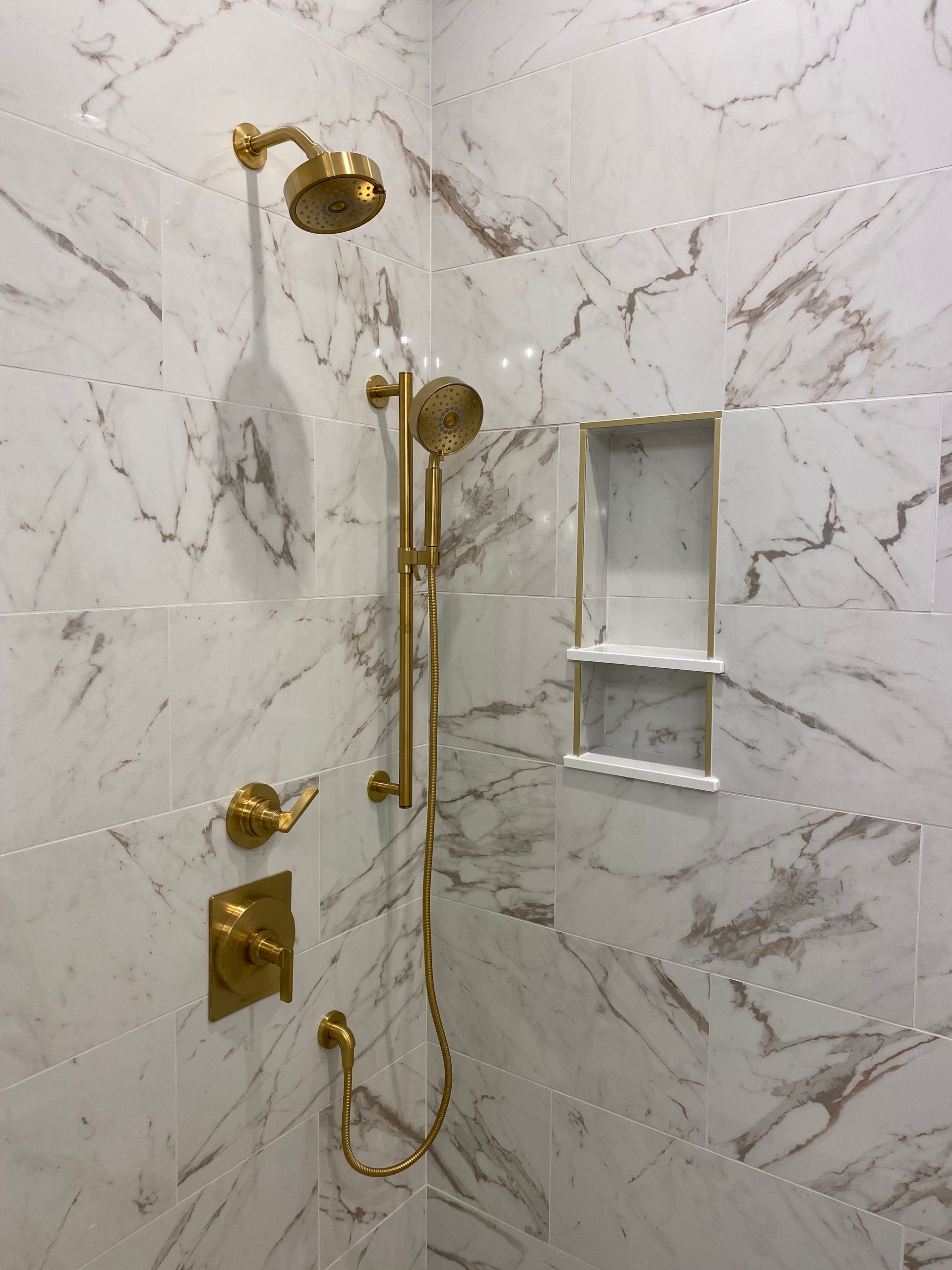 Vibrant brushed modern brass Kohler Castia plumbing fixtures in shower with custom niche.