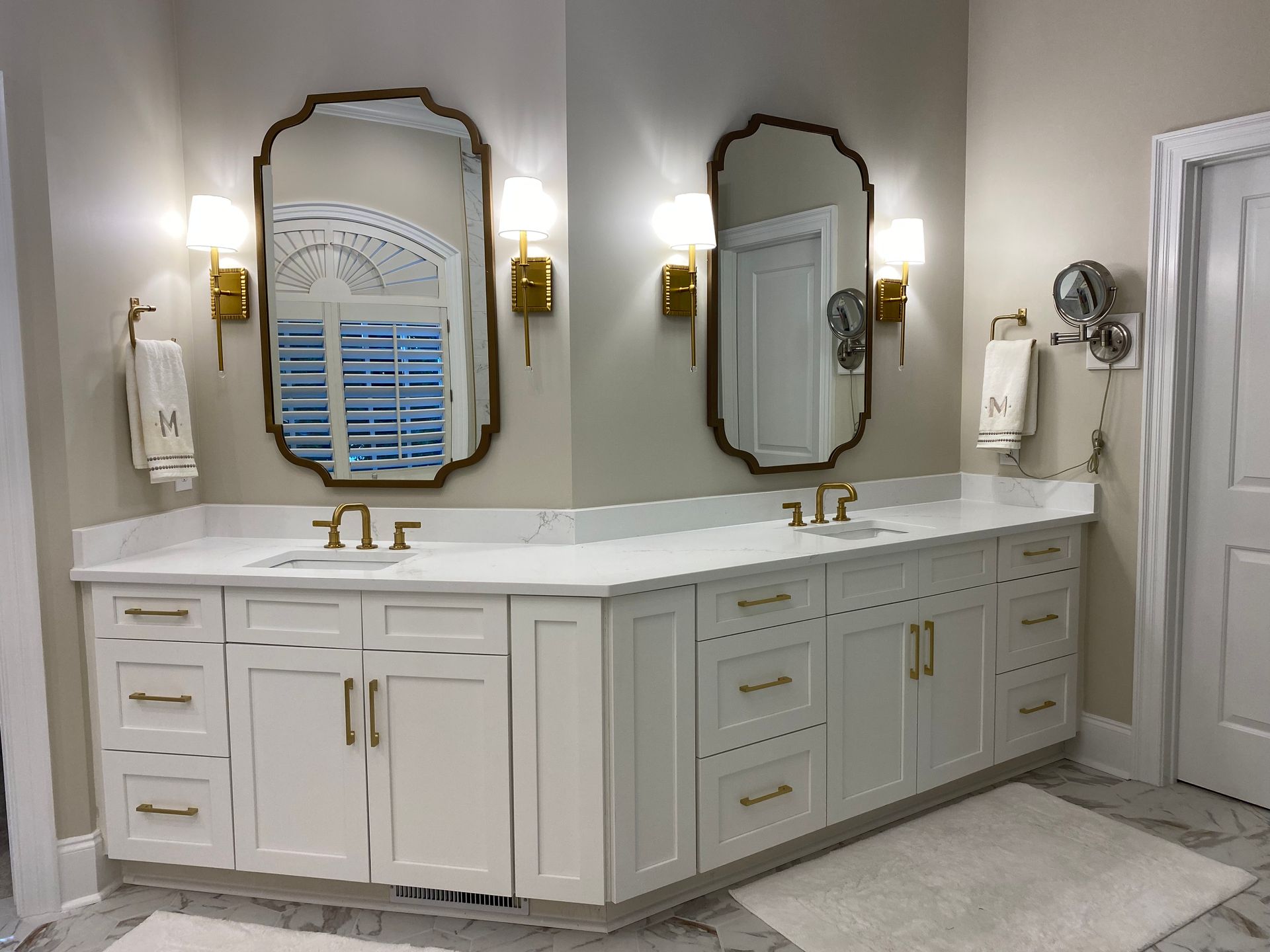 White oversized his and hers bathroom vanity with gold fixtures and rectangular under-mount sinks.