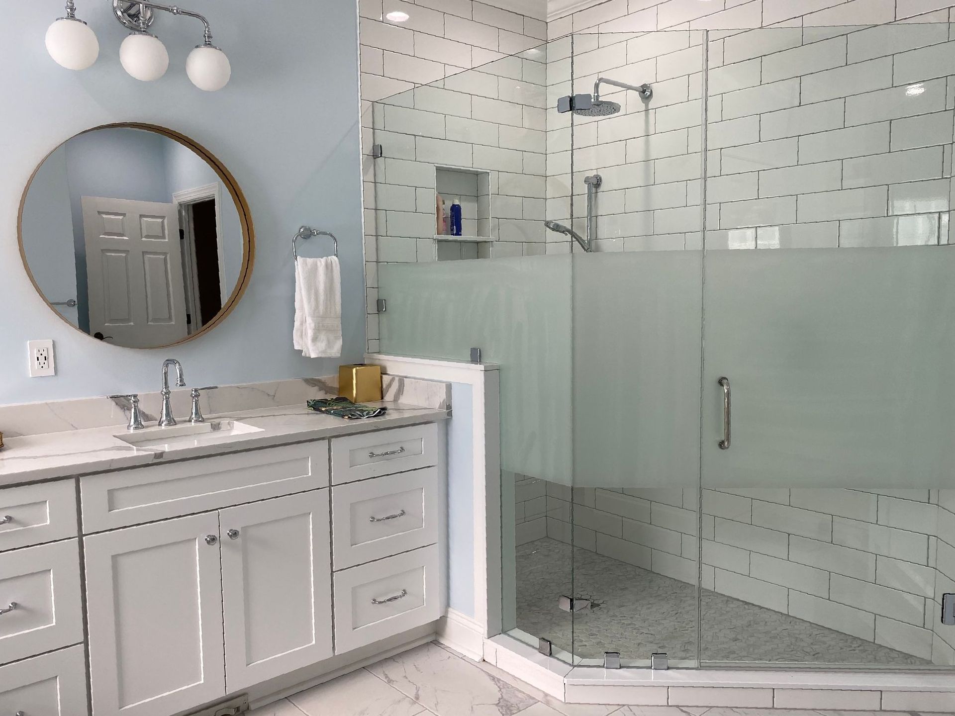 Walk-in tiled shower with frosted privacy glass next to a white shaker vanity.