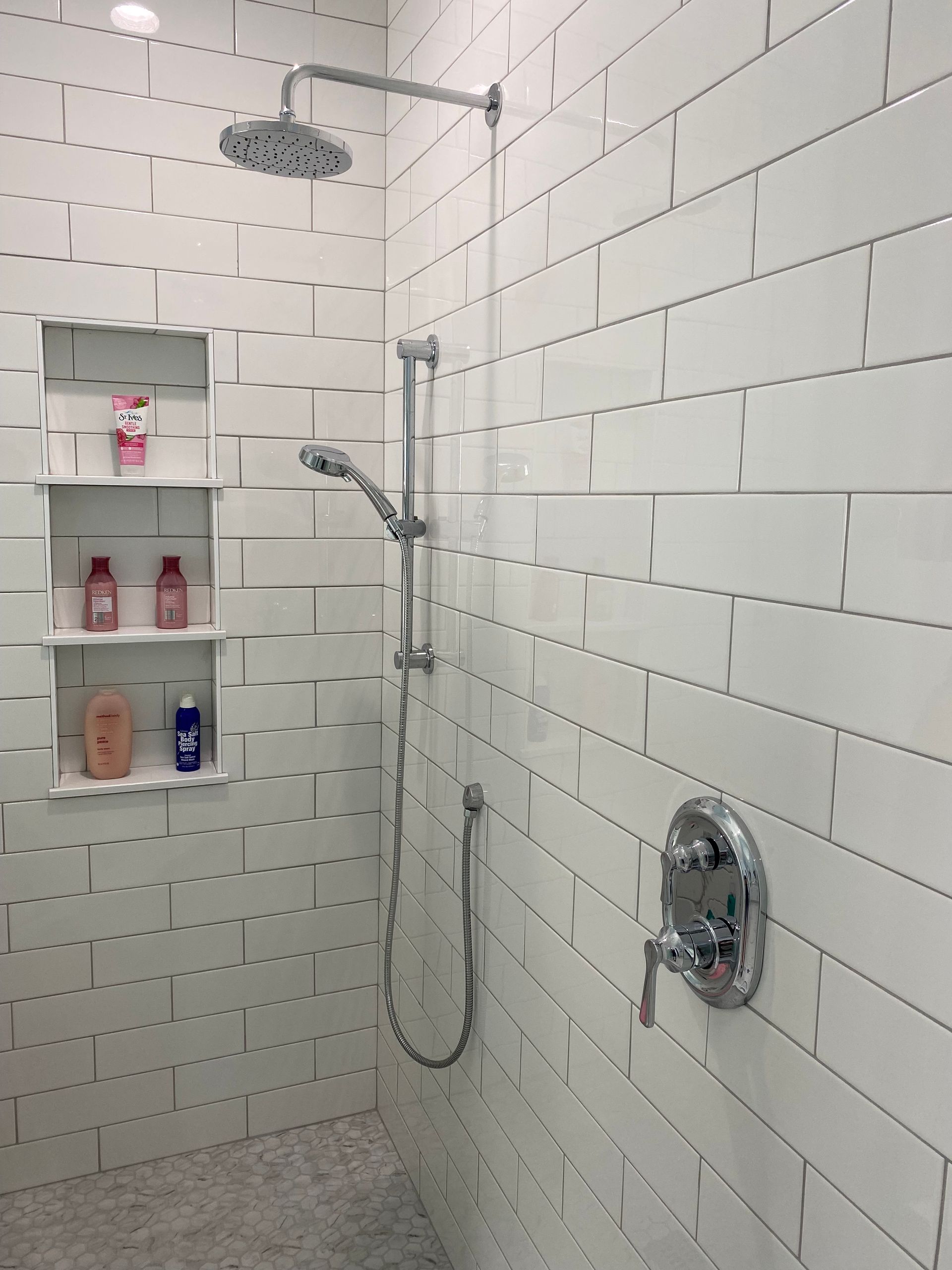 Custom three tiered wall niche in white tiled shower.