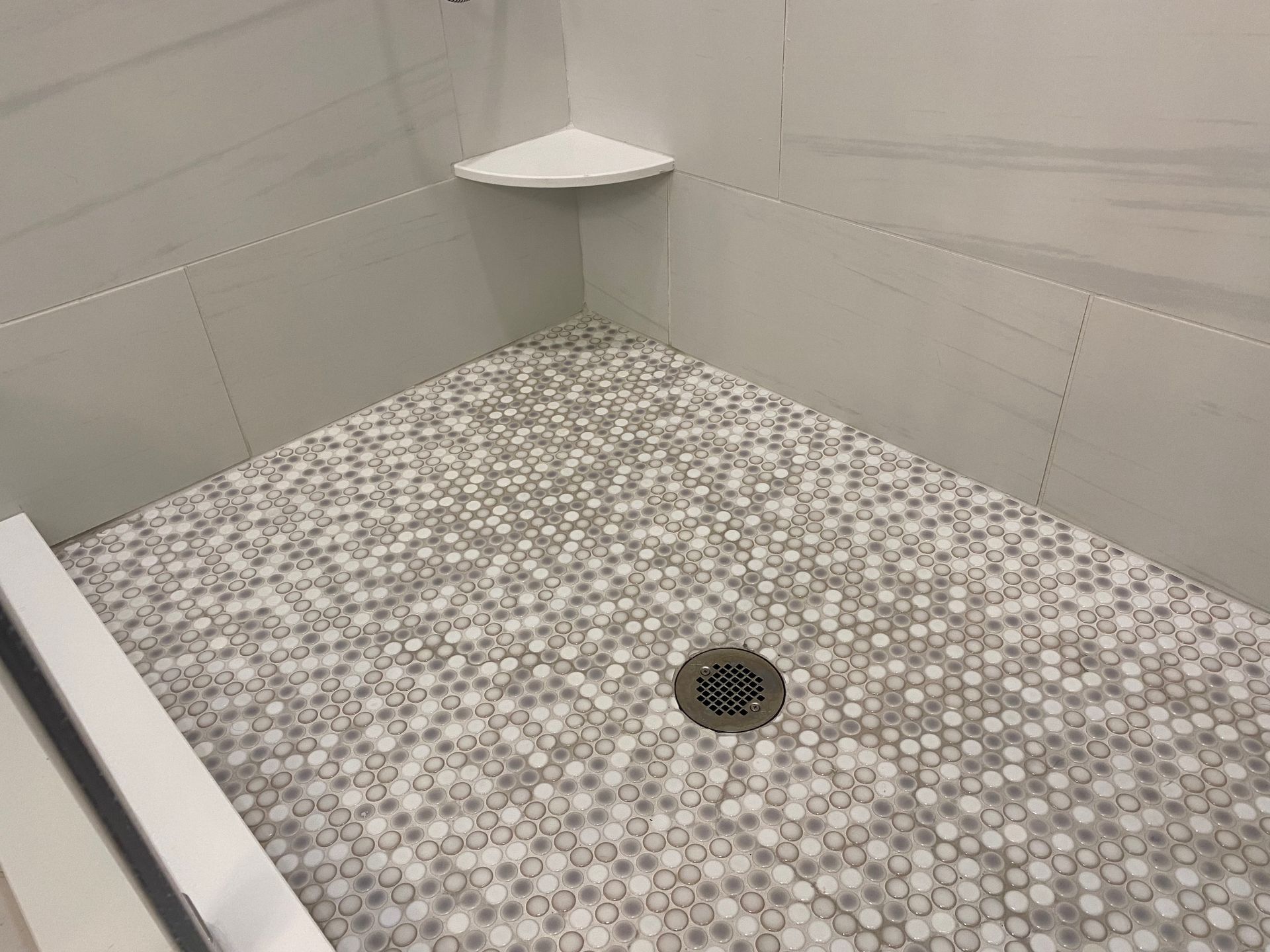 Small circular grey and white tiled shower floor with built-in shower shelf.