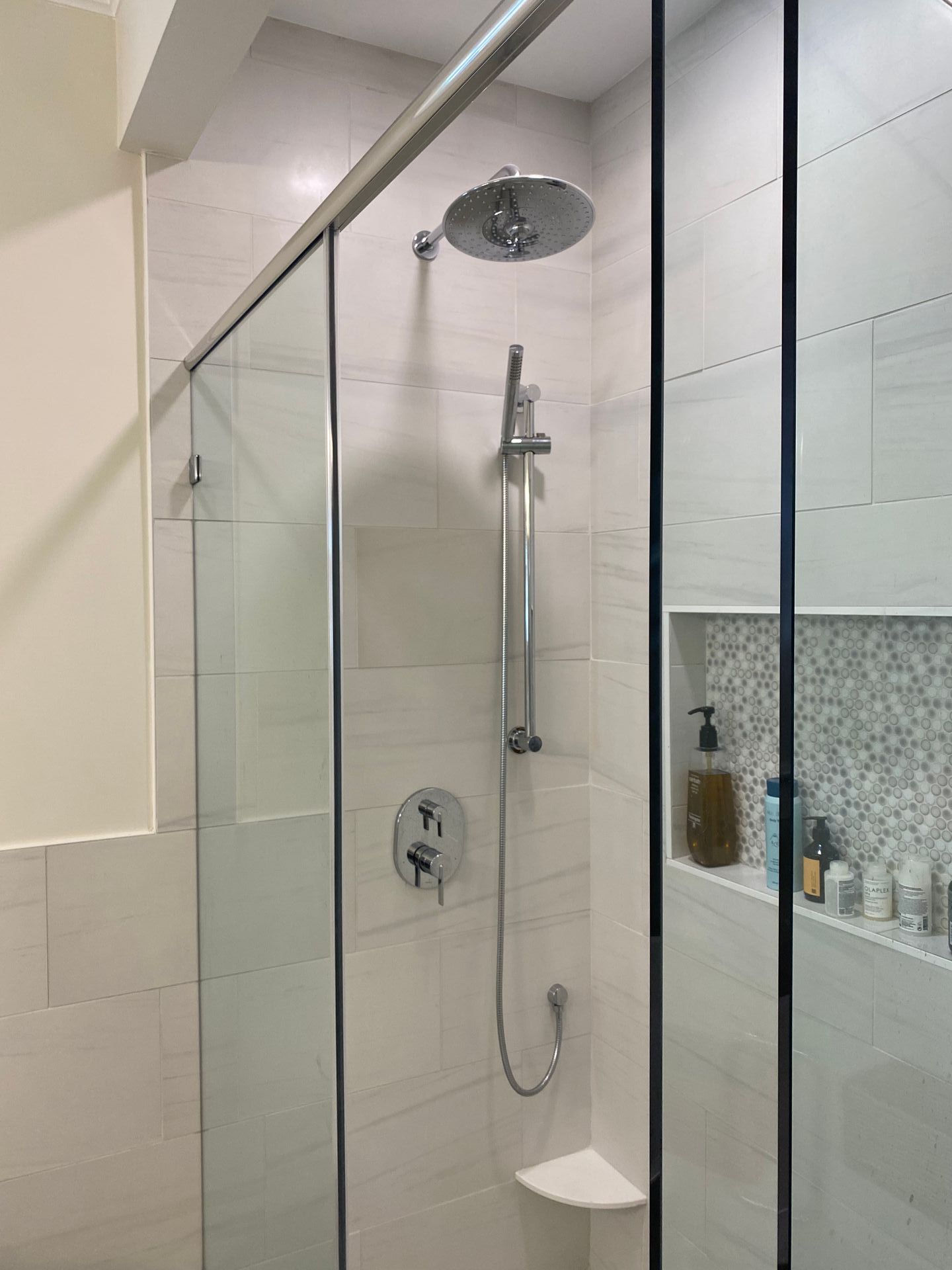Handheld sprayer on slide bar with rainhead shower feature with oversized wall niche in bathroom remodel.