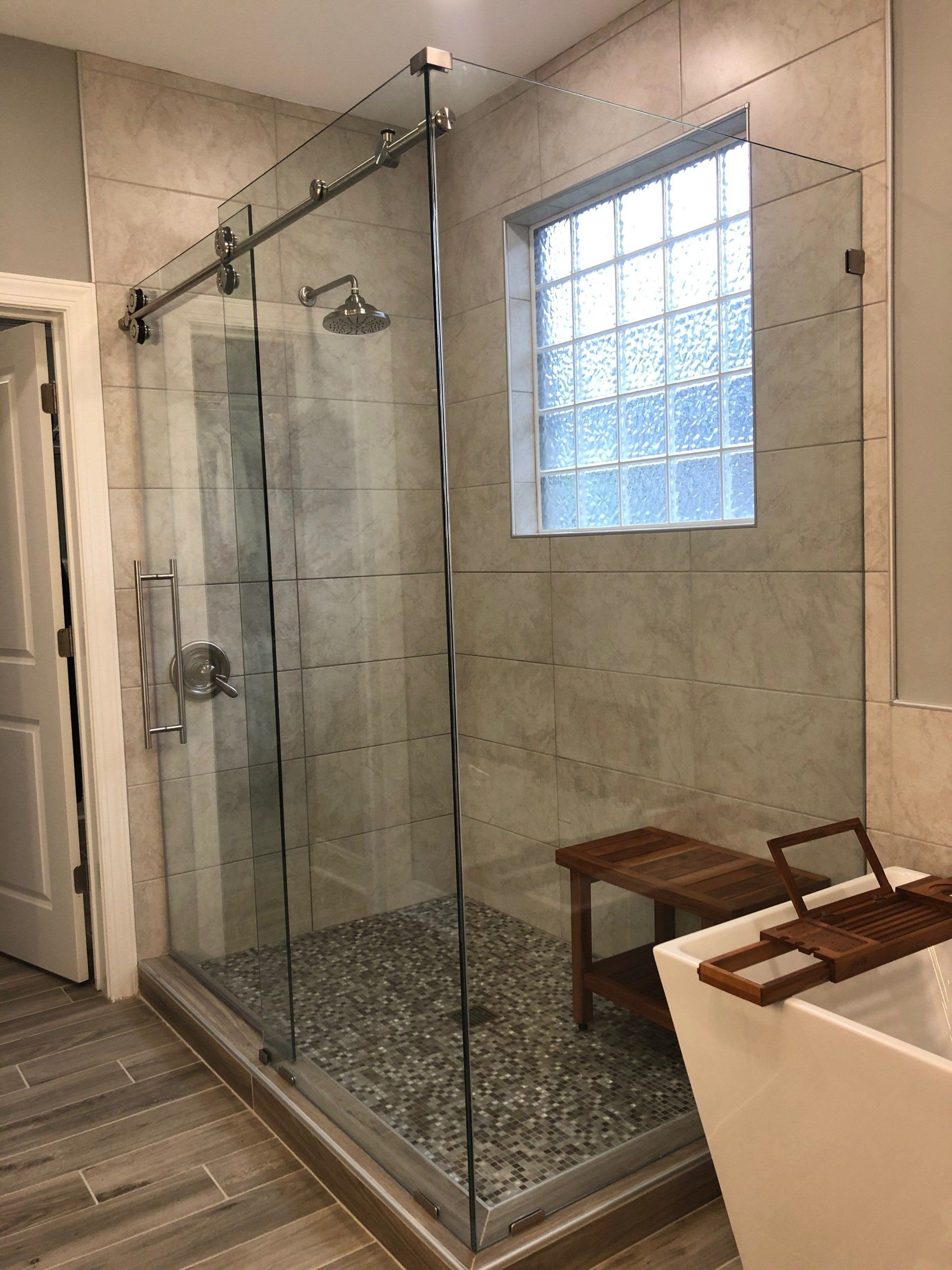 Walk-in shower with polished stainless roller barn style shower door and glass mosaic patterned tile shower floor.