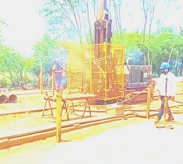 Um homem com capacete está parado em frente a uma máquina.