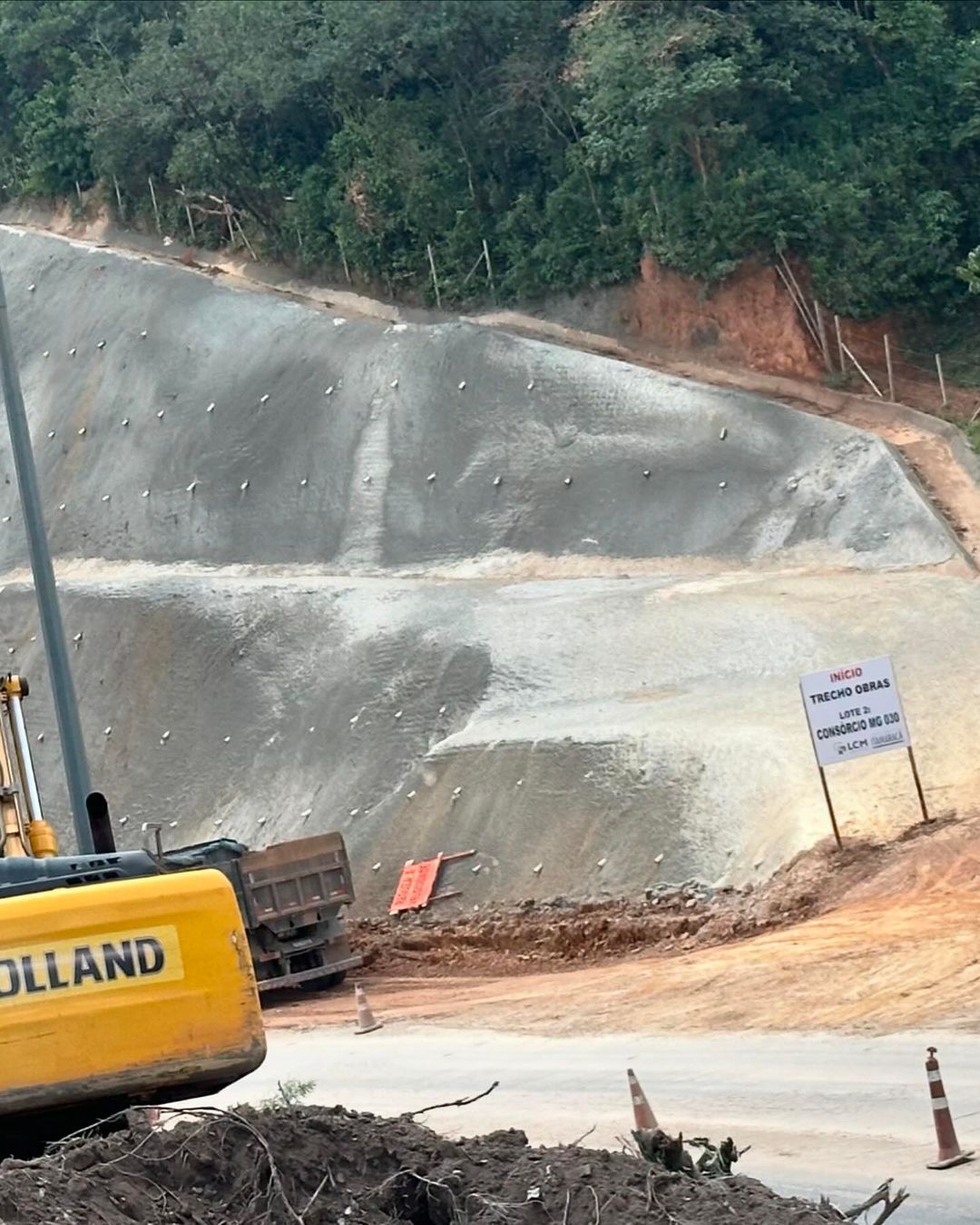 Uma escavadeira amarela está em cima de uma pilha de terra ao lado de uma estrada.