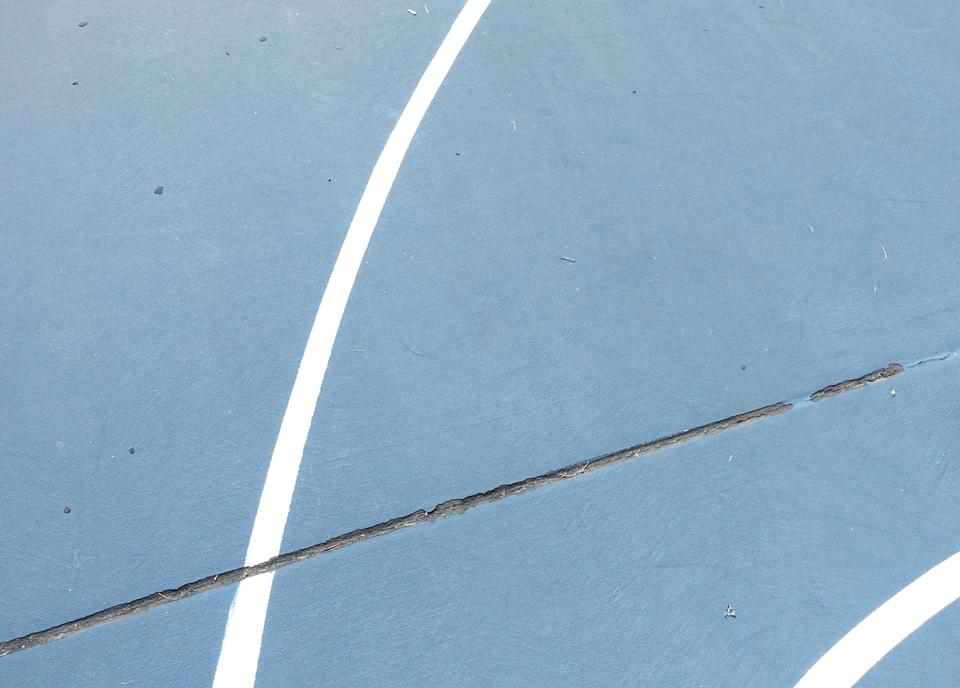 Blue sport court surface with white lines and a crack.