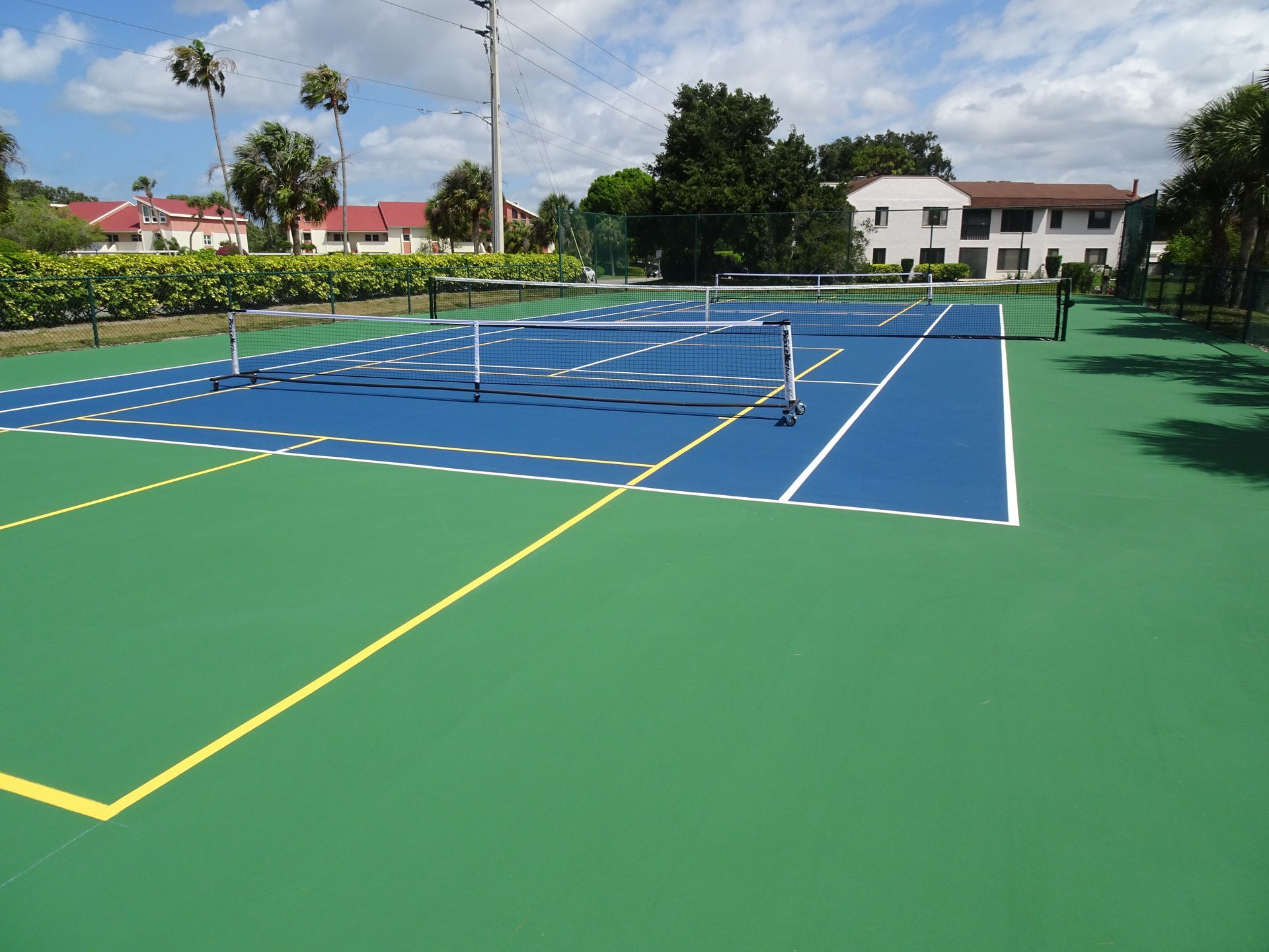 Basketball court with blue, gray, and orange paint, set in a park on a sunny day.