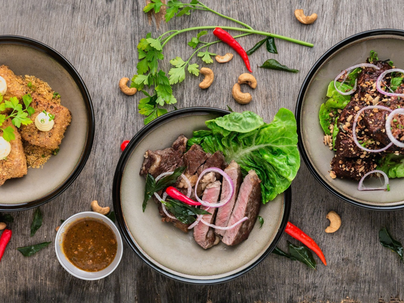 Three plates of food are sitting on a wooden table.