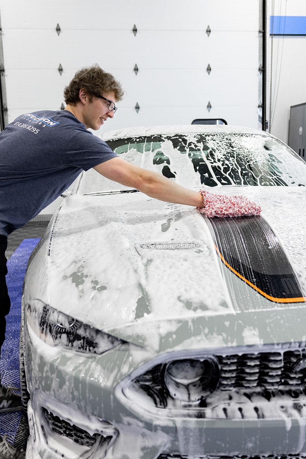 A man is washing a car with foam in a garage.