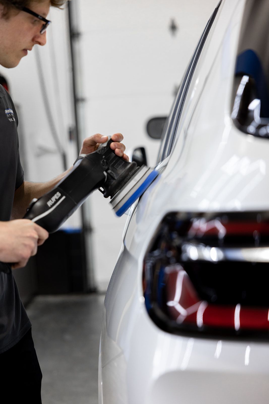 A man is polishing a white car with a machine.
