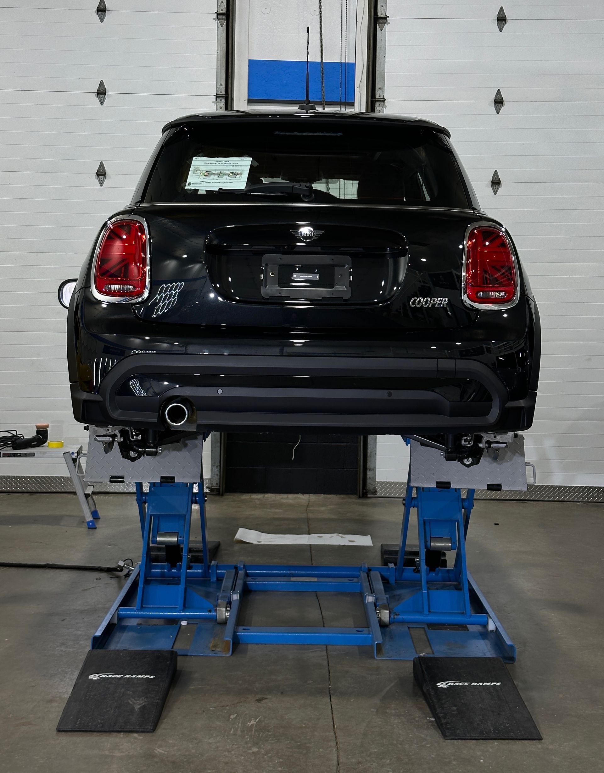 A black mini cooper is sitting on a lift in a garage.