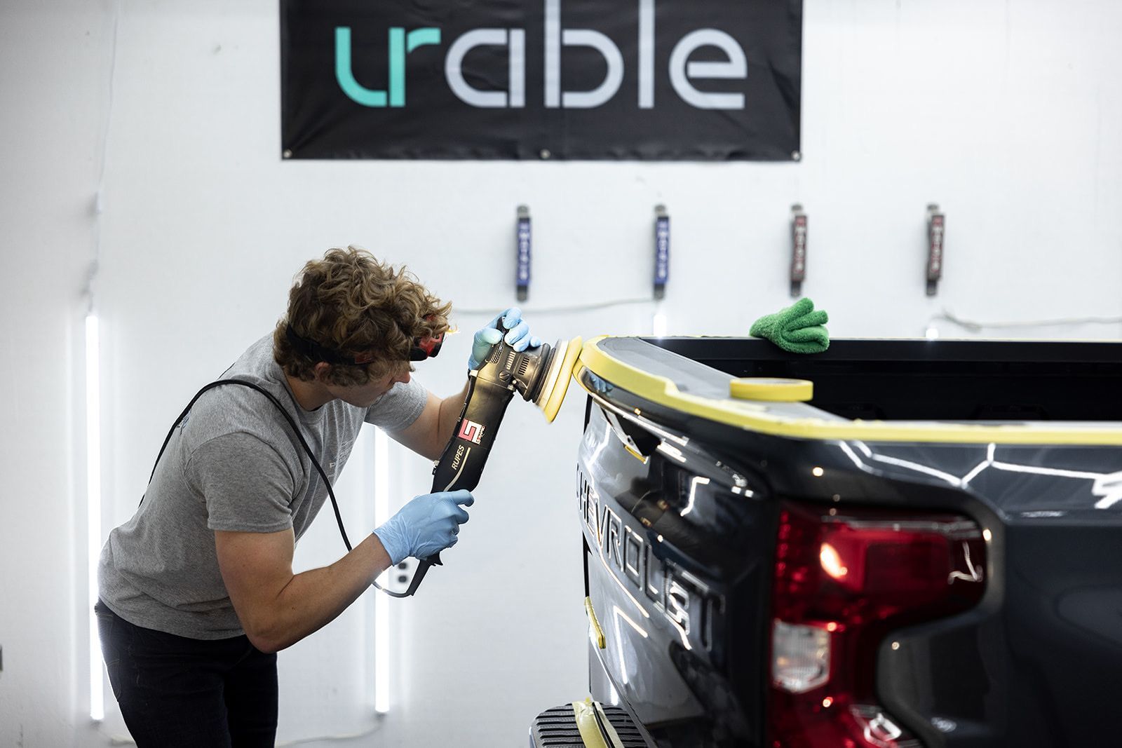 A man is polishing the back of a truck in a garage.
