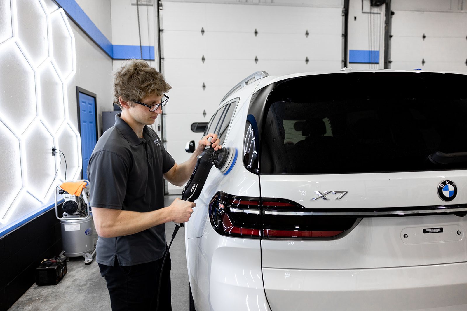 A man is polishing a white bmw x7 in a garage.