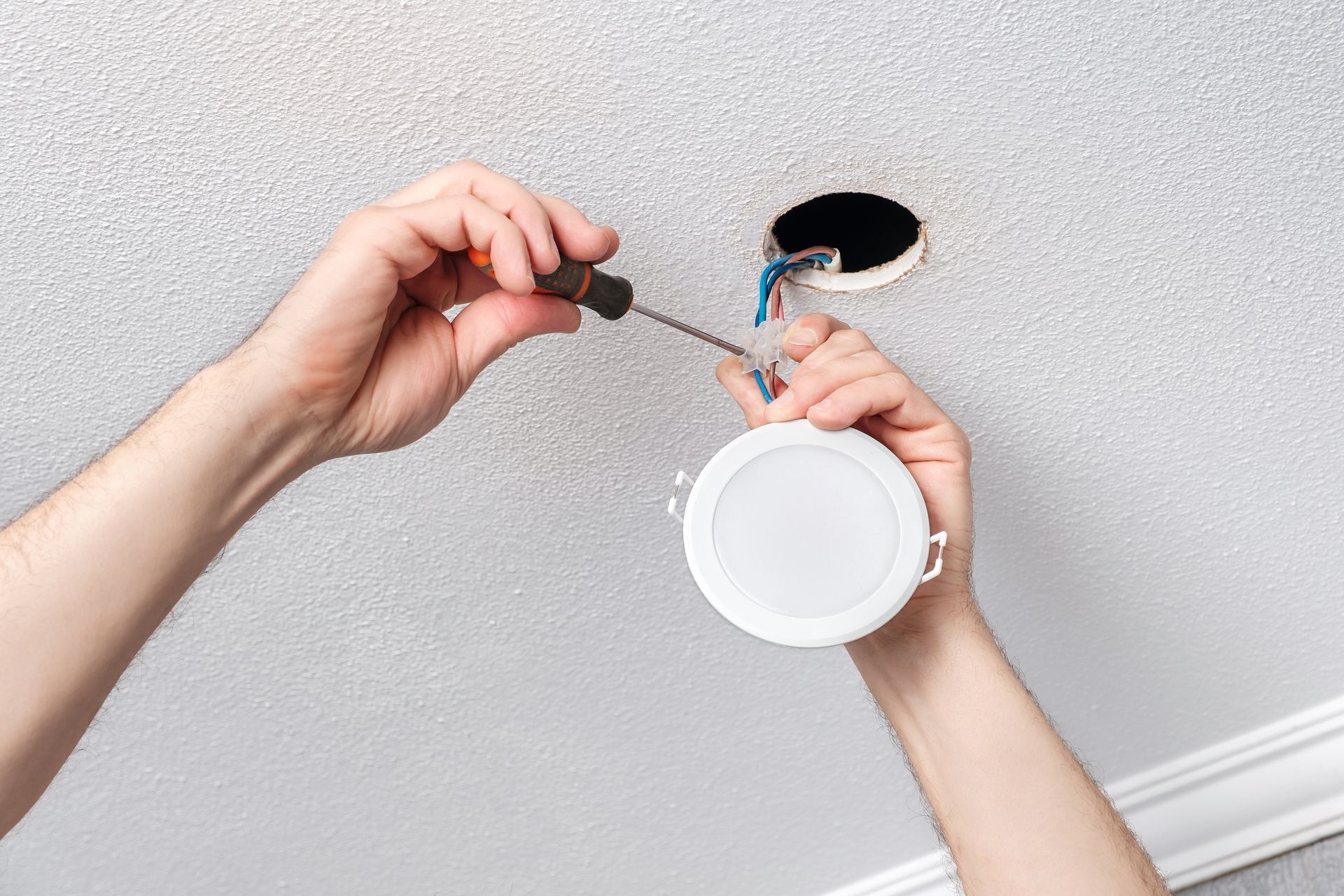 A person is installing a light fixture in the ceiling with a screwdriver.