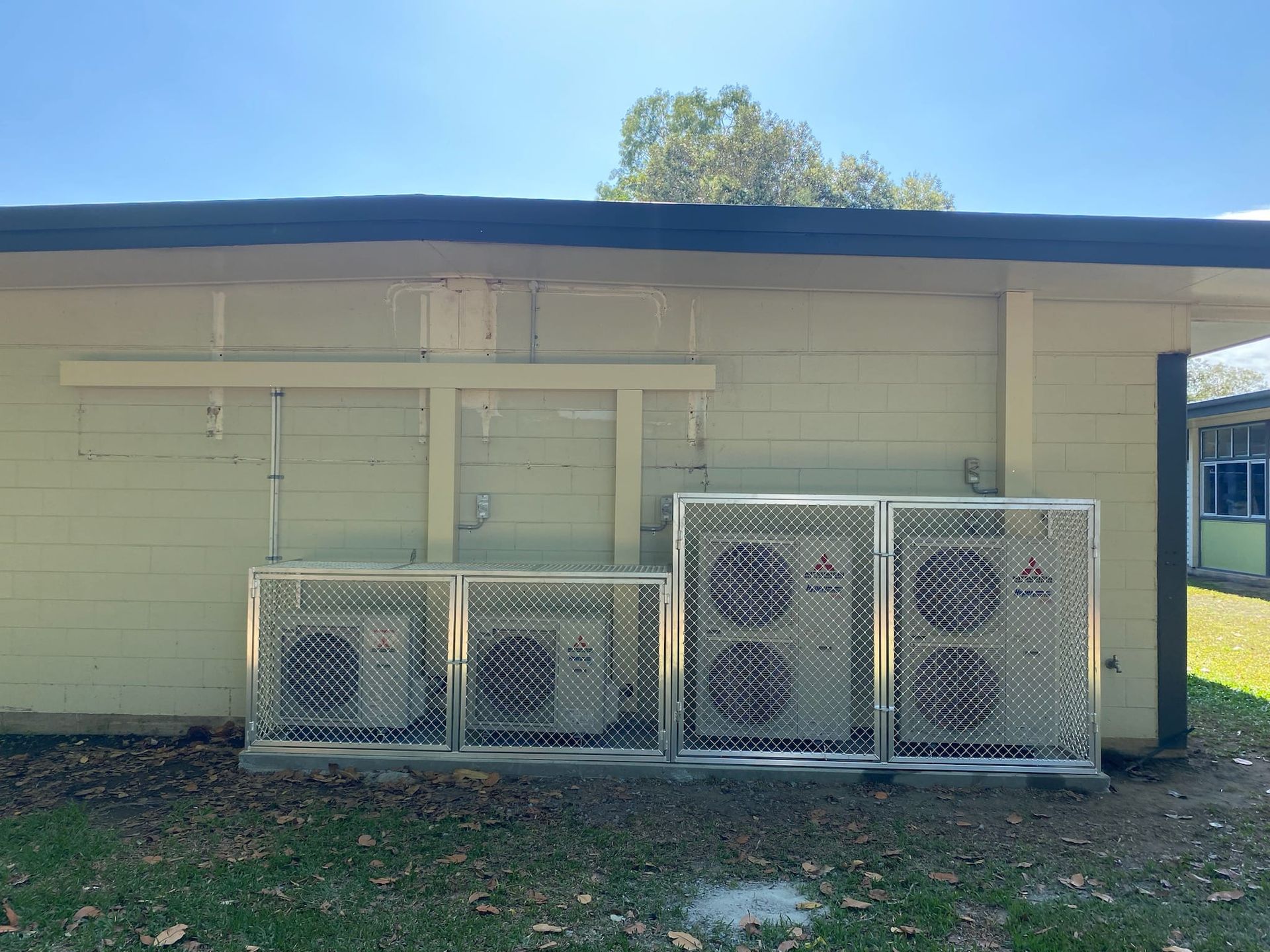Air Conditioning Units Enclosed in Metal Cages Against a Beige Building Exterior — Mingweld Fabrication in Bungalow, QLD