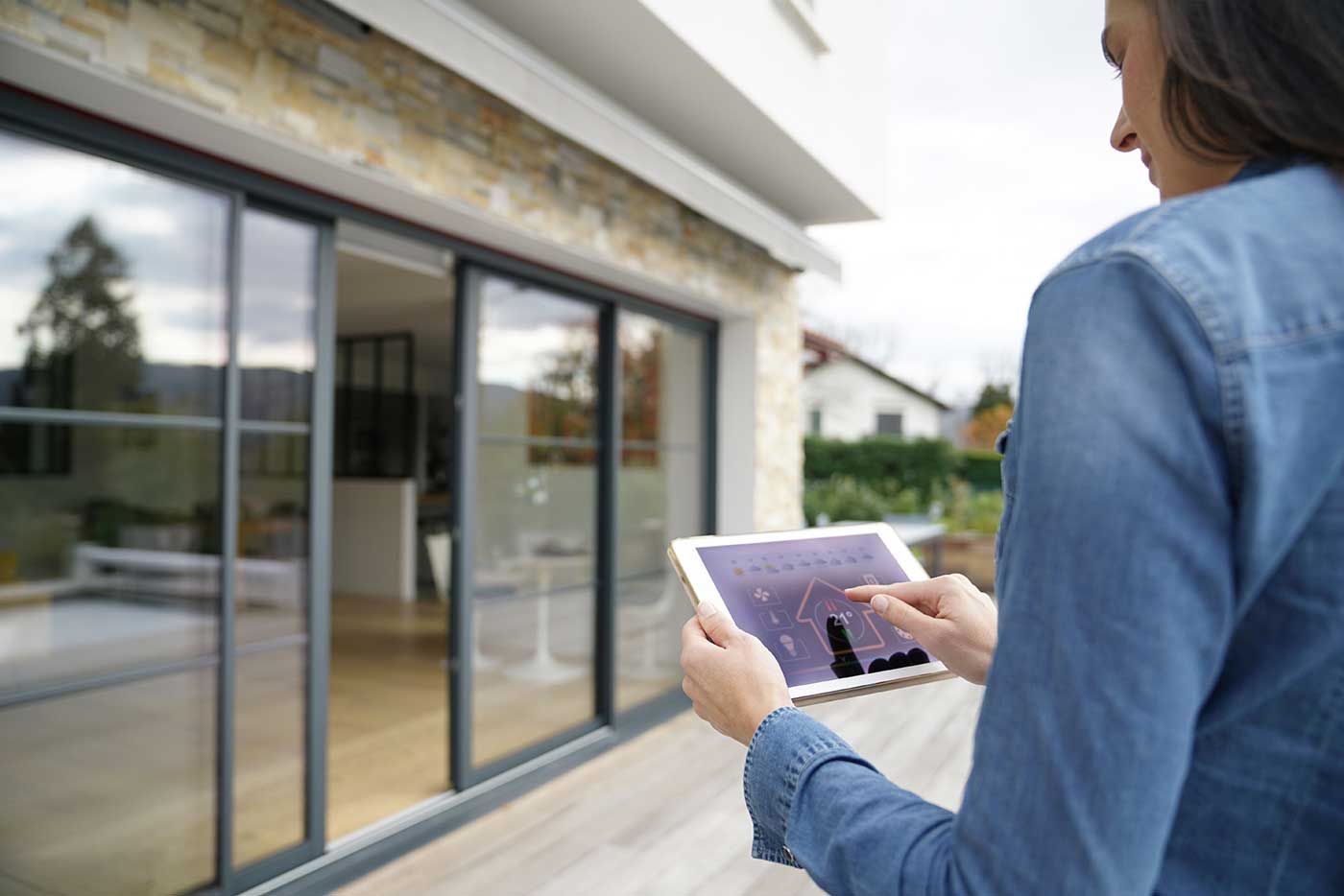 A woman is holding a tablet in front of a house.