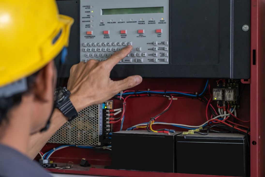 A man wearing a hard hat is working on a fire alarm system.