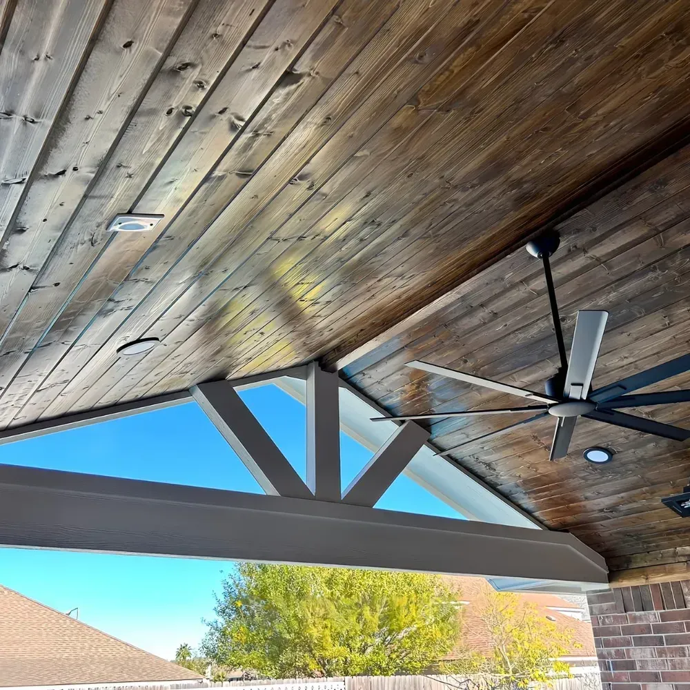 Wooden patio ceiling with a fan and sky visible through a triangular opening.