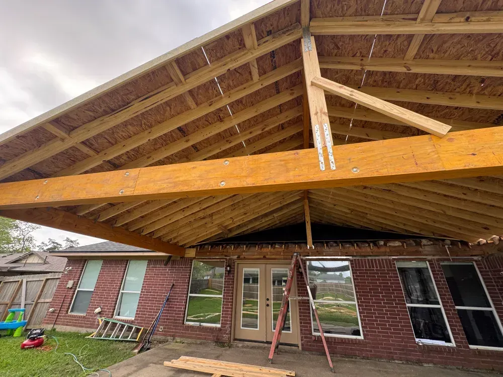 Construction of a new roof over a brick house.  Wooden beams and support structures are visible.