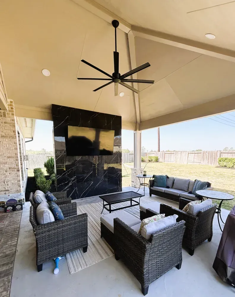 Covered patio with seating, TV, black accent wall, and large ceiling fan.