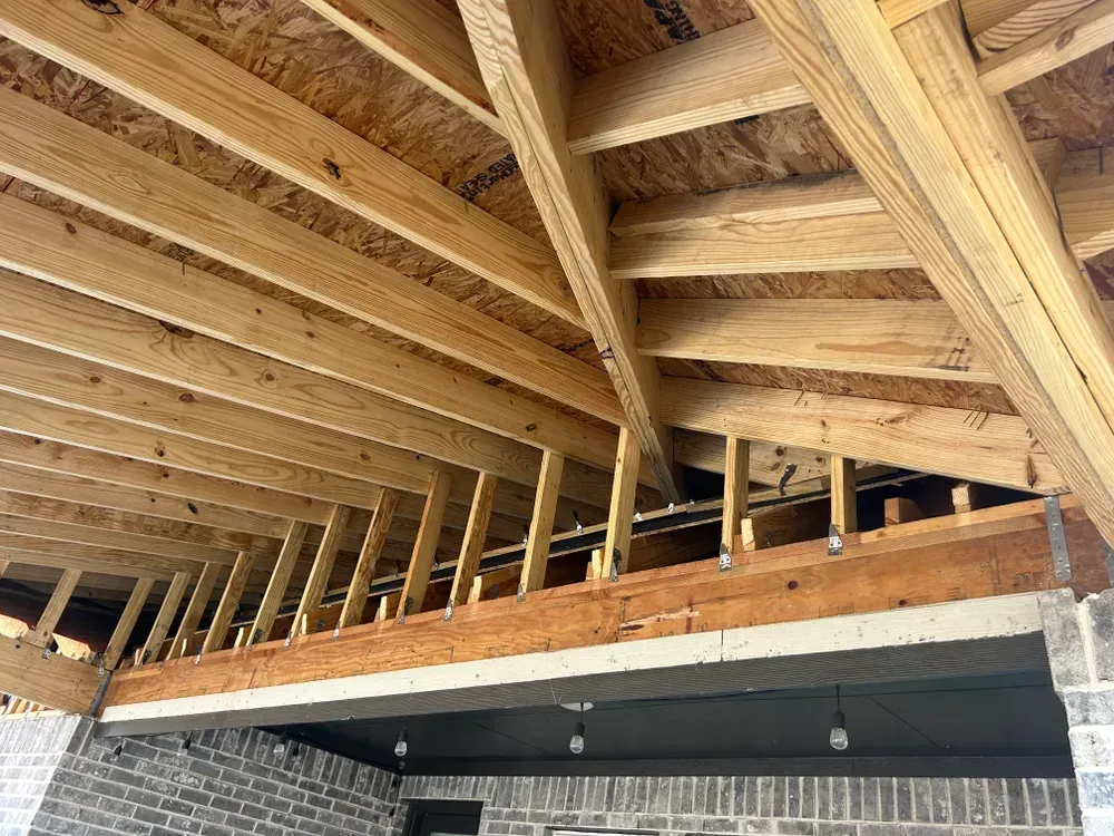 Wooden roof framing over a brick structure, with exposed beams and rafters.