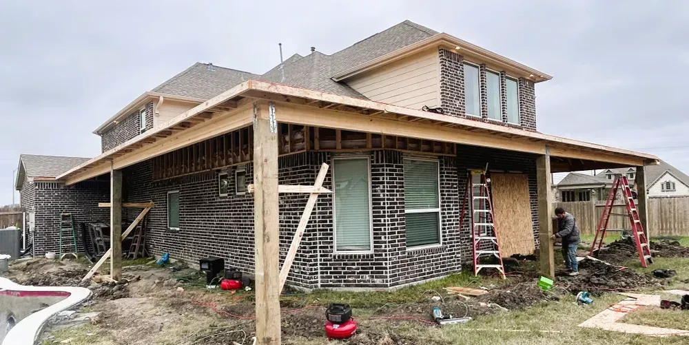 Construction of a porch on the back of a house. A worker and a ladder are visible. Overcast day.