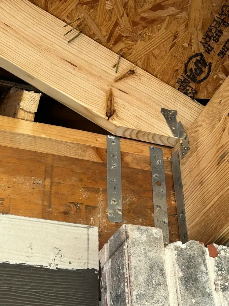Wooden roof truss construction, with metal straps connecting to brick and lumber.