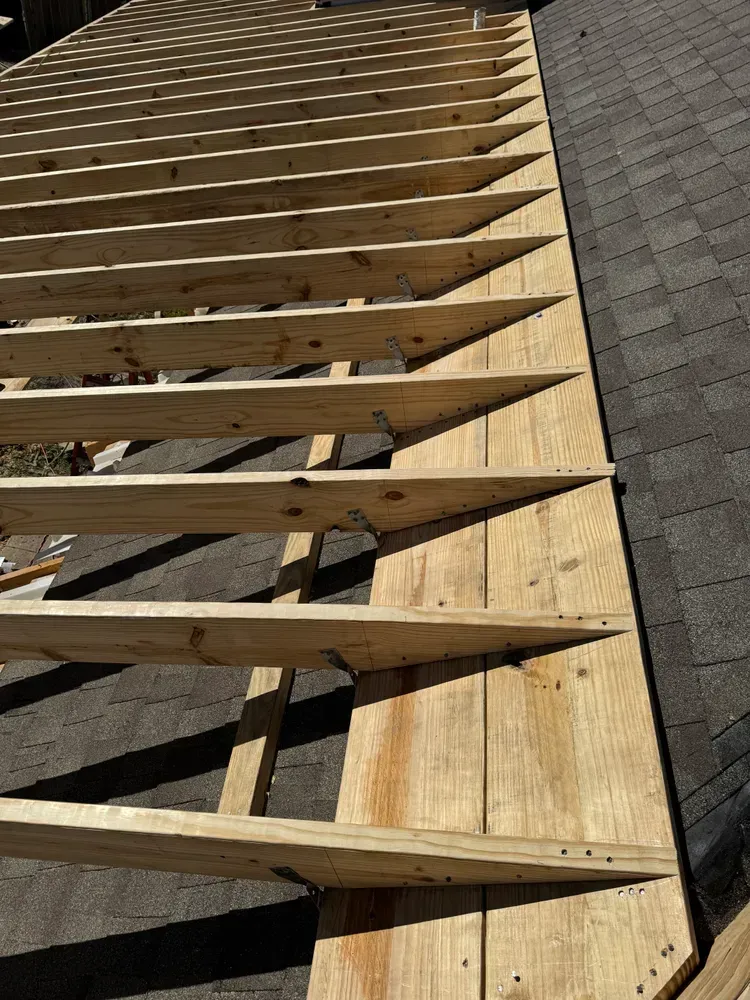Wooden roof frame being built on a dark shingled roof.