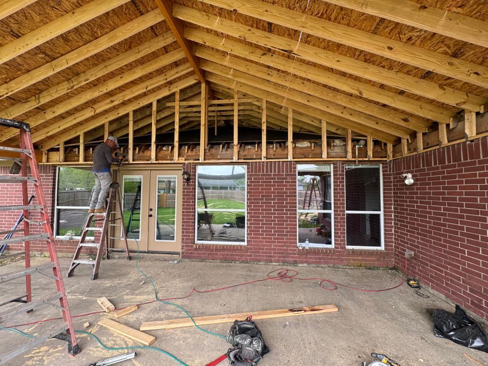 Construction of a patio cover attached to a brick house. A worker is on a ladder.