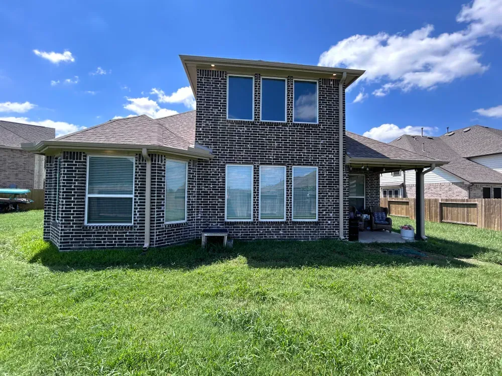 Back of a house with exposed brick siding, windows, and a grassy yard under a blue sky.