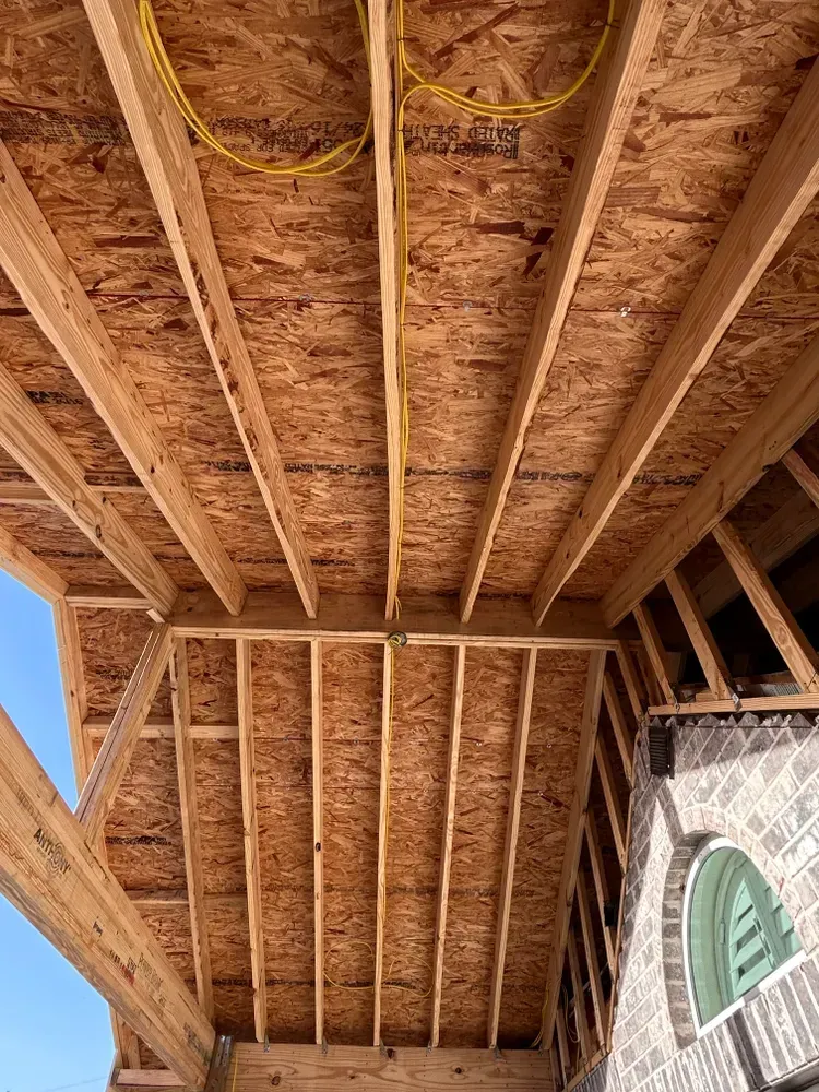 Wooden construction of a sloped roof with exposed beams and electrical wiring.