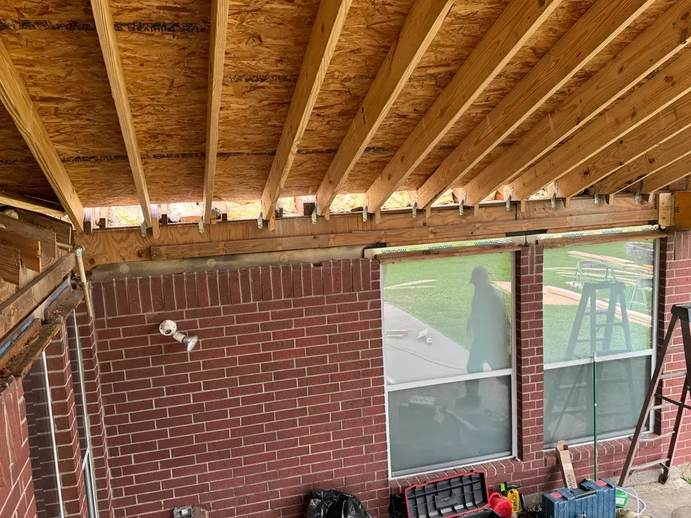 Brick wall with windows, under construction patio roof. Man visible through window.