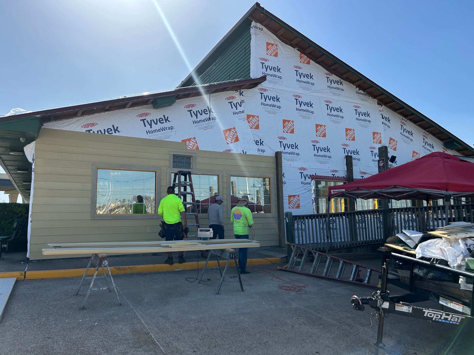 Construction workers installing siding on a building with Tyvek wrap; sunny day.