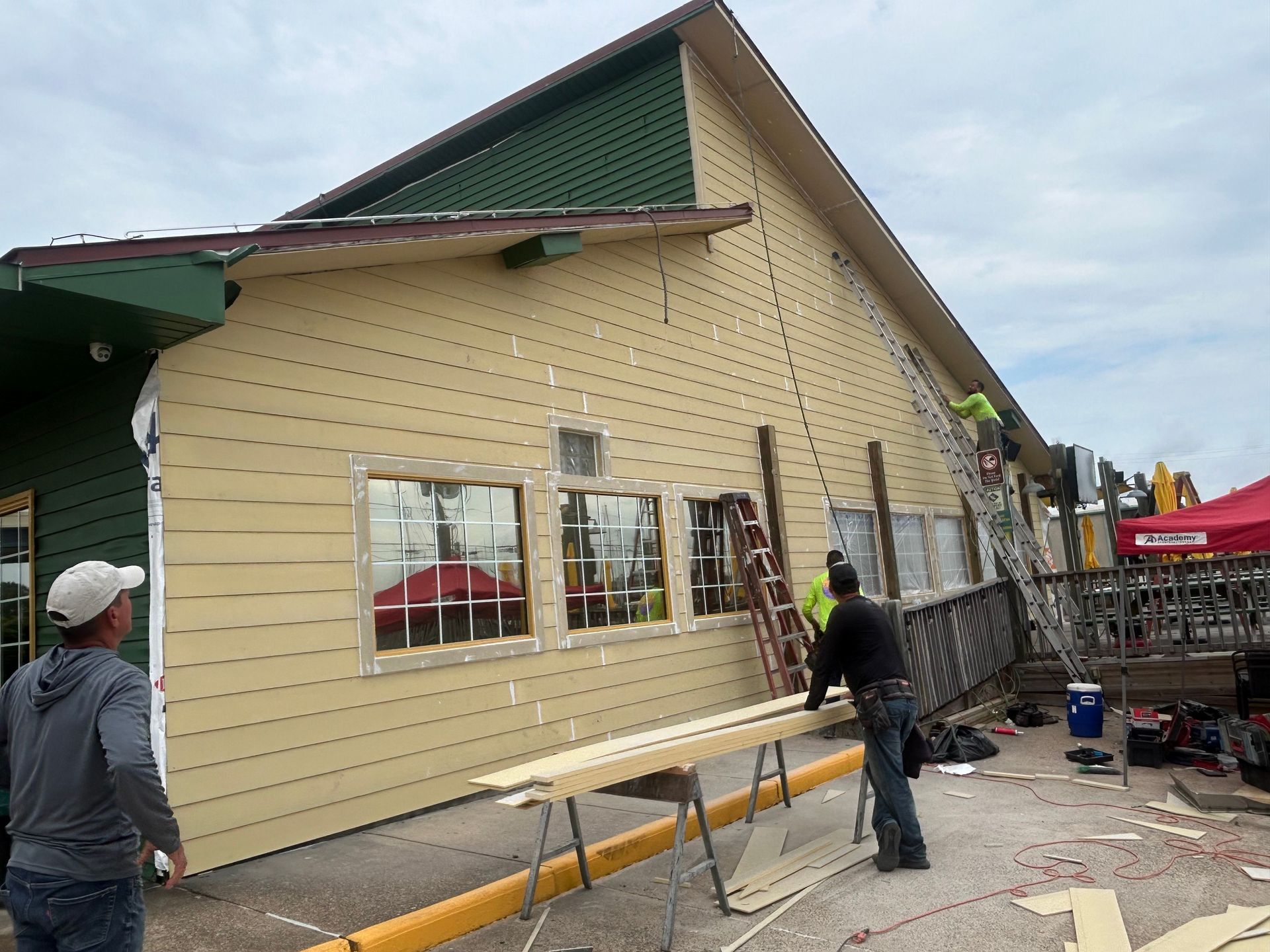 Construction workers installing siding on a tan building with green trim.