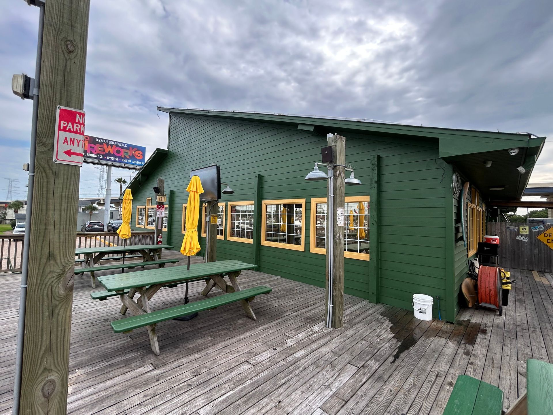 Green building with yellow umbrellas, picnic tables, and wooden deck. Sign says “No Parking”.