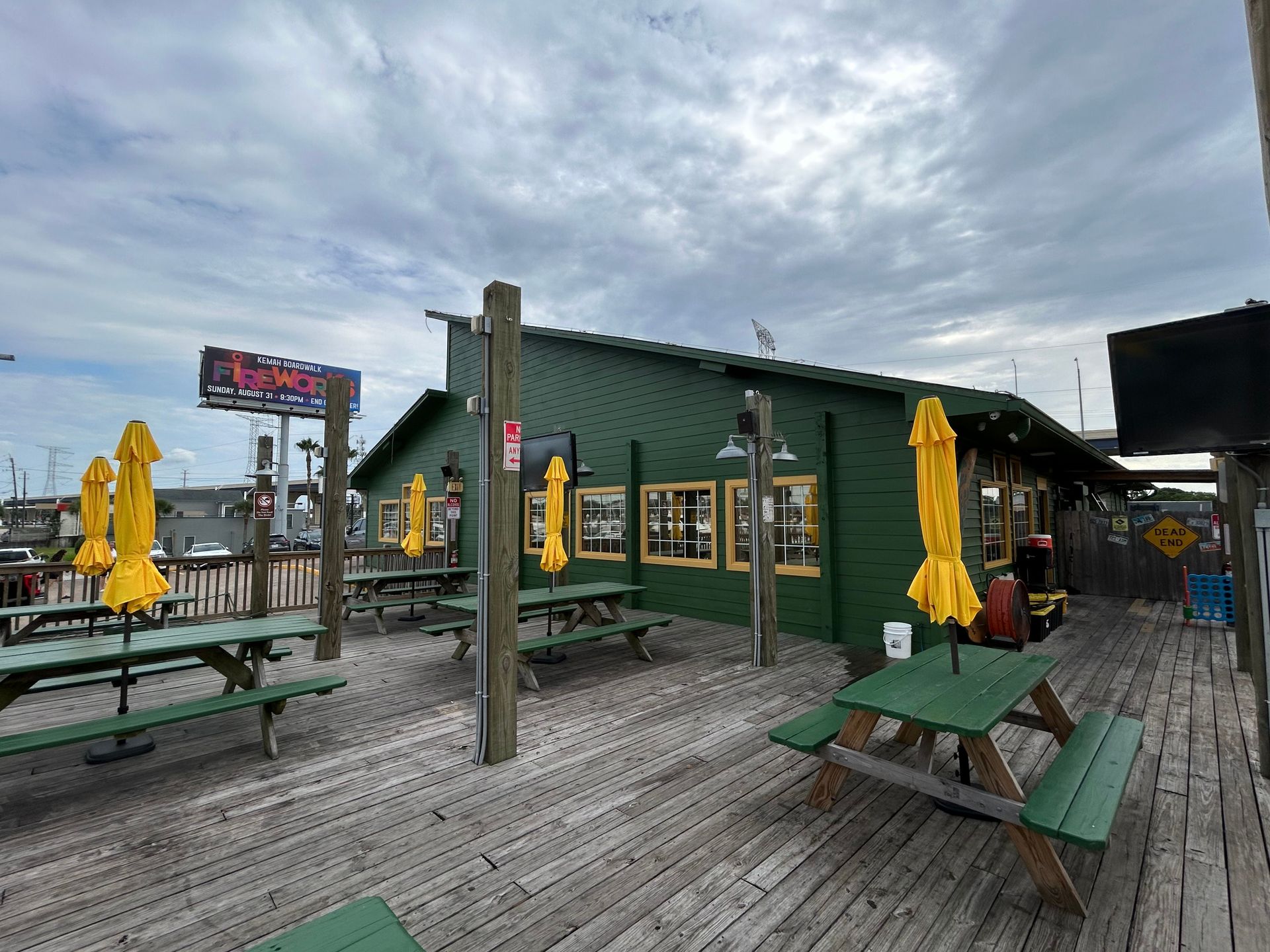 Green restaurant with wooden deck and yellow umbrellas on a cloudy day.