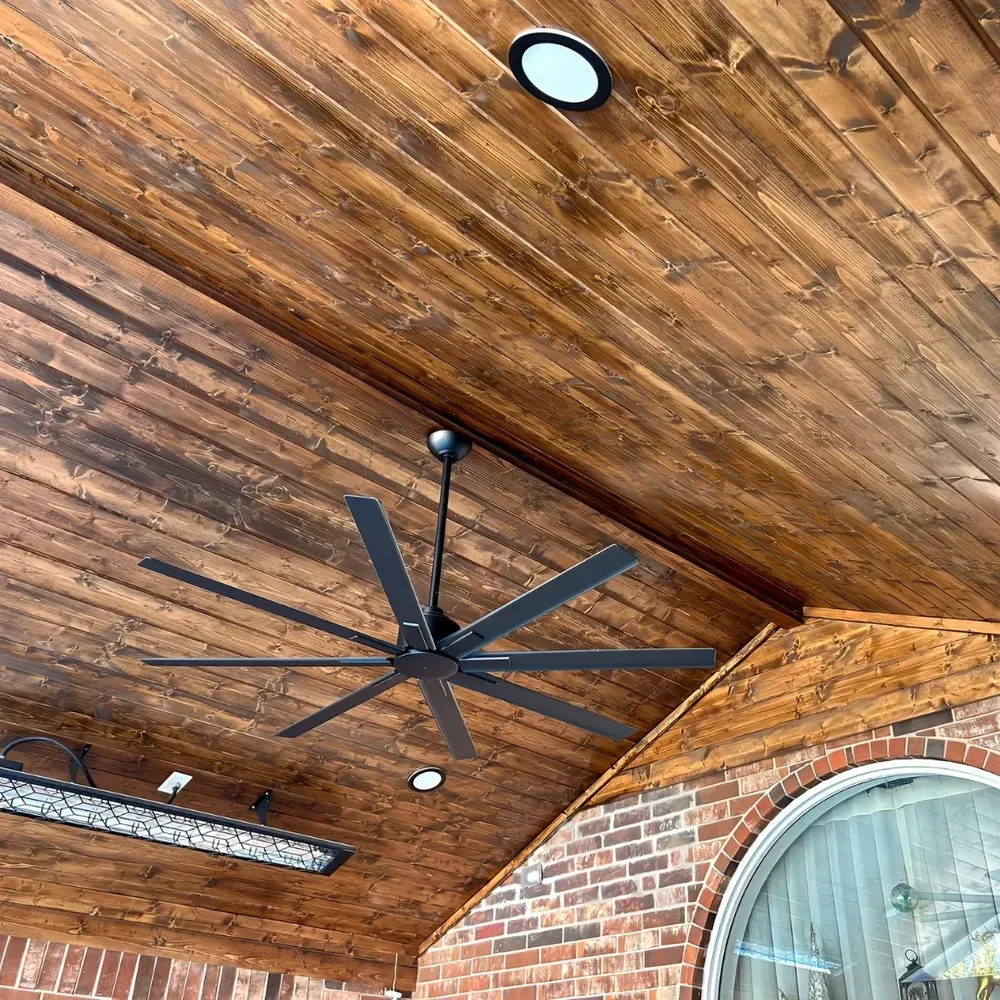 Wooden patio ceiling with a black ceiling fan, lights, and brick accents.