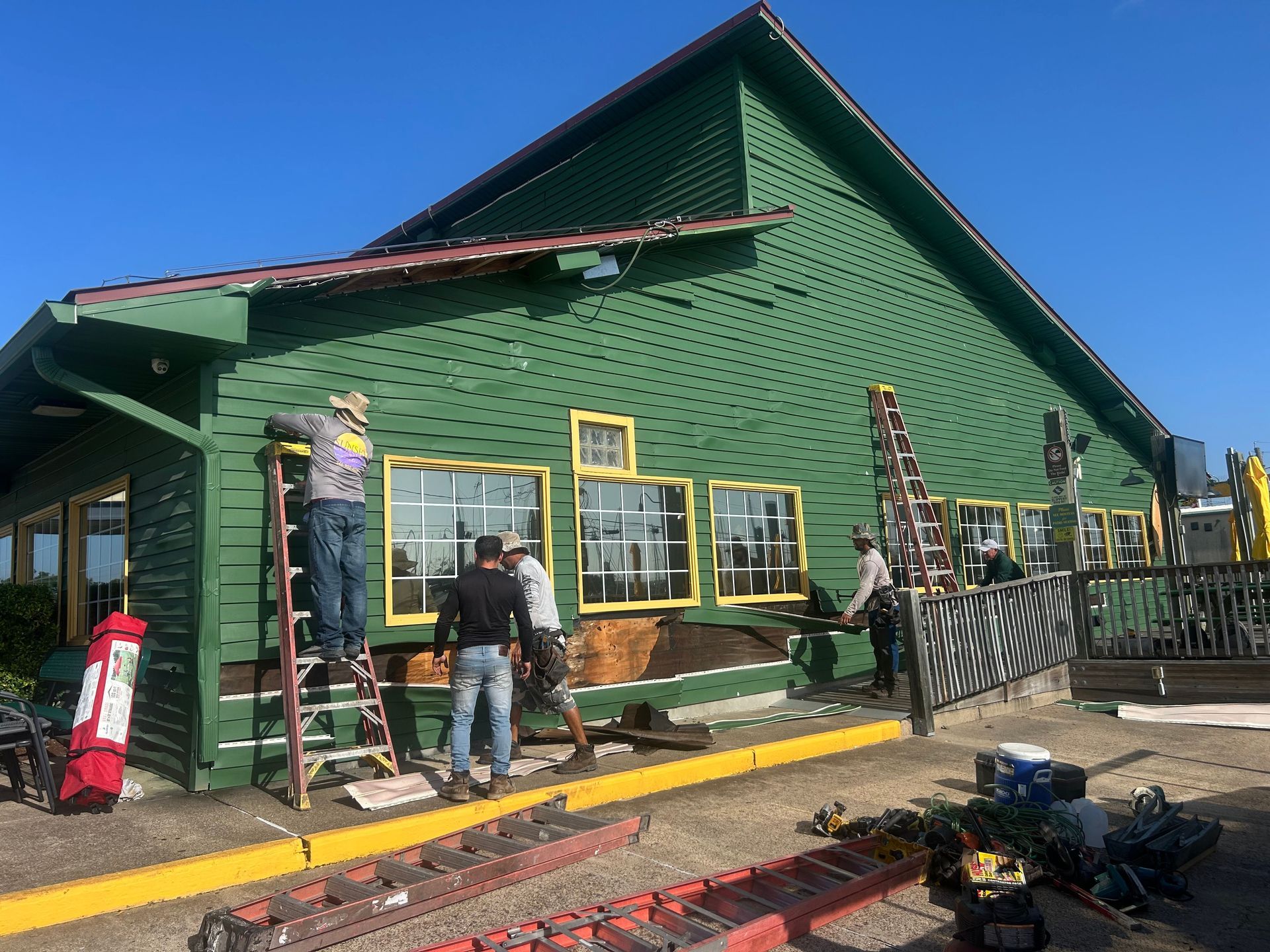 Construction workers repairing a green building with yellow trim; sunny outdoors.