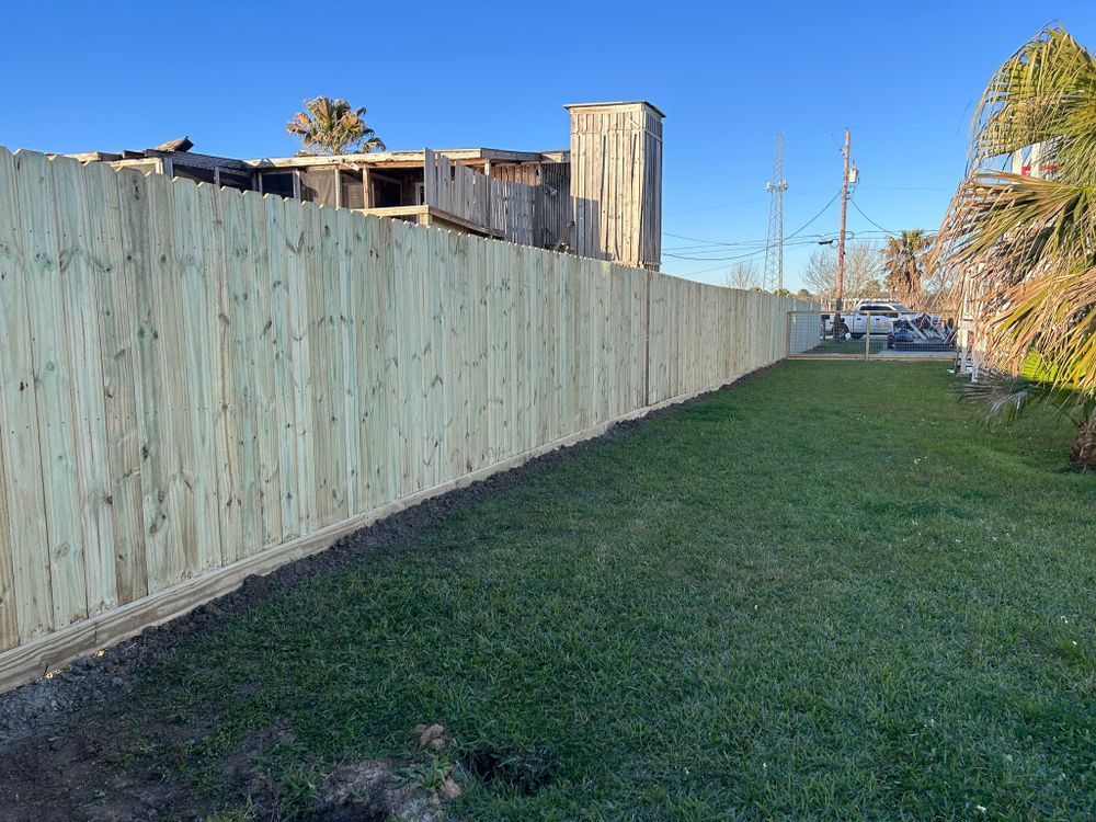 Wooden fence in front of a green lawn, with a building in the background on a sunny day.