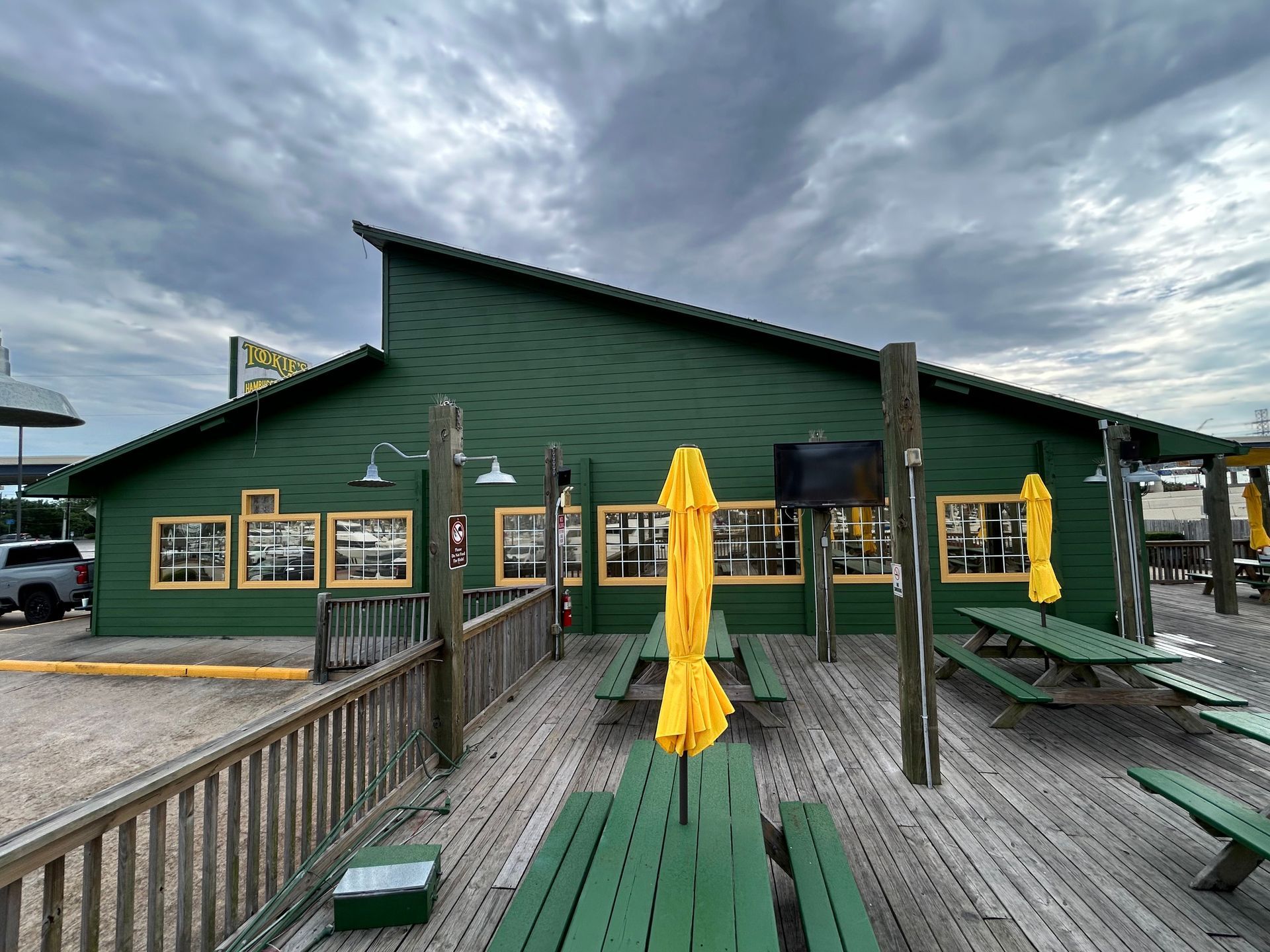 Green restaurant with outdoor seating under a cloudy sky. Yellow umbrellas and green picnic tables.
