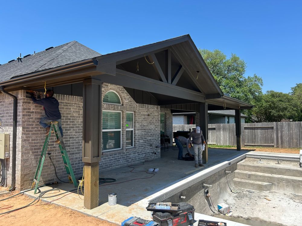 Construction of a covered patio next to a pool. Workers, brick house, blue sky.